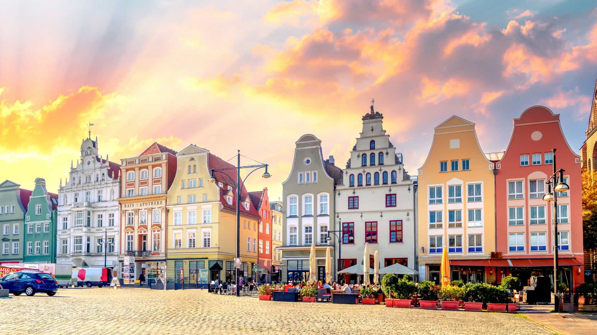 Historic gabled buildings in Rostock’s Old Town line a cobblestone square, with pastel façades, outdoor cafés, and warm sunset light illuminating the scene.