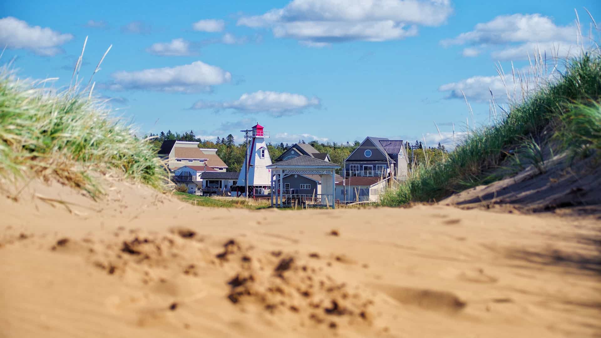 A fun, close-up view of the famous World's Largest Lobster statue in Shediac, New Brunswick, Canada—a popular maritime shore excursion destination known as the "Lobster Capital of the World." The image captures the massive, highly detailed sculpture of a giant Atlantic lobster resting on a stone pedestal, flanked by Canadian and provincial flags under a bright blue sky.