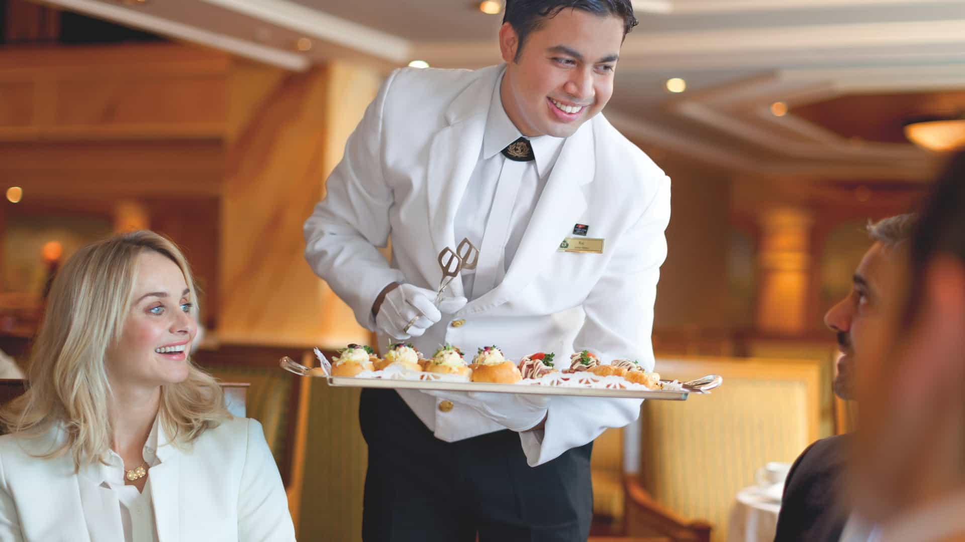 A smiling staff member serving afternoon tea on Cunard's Queen Victoria ship.