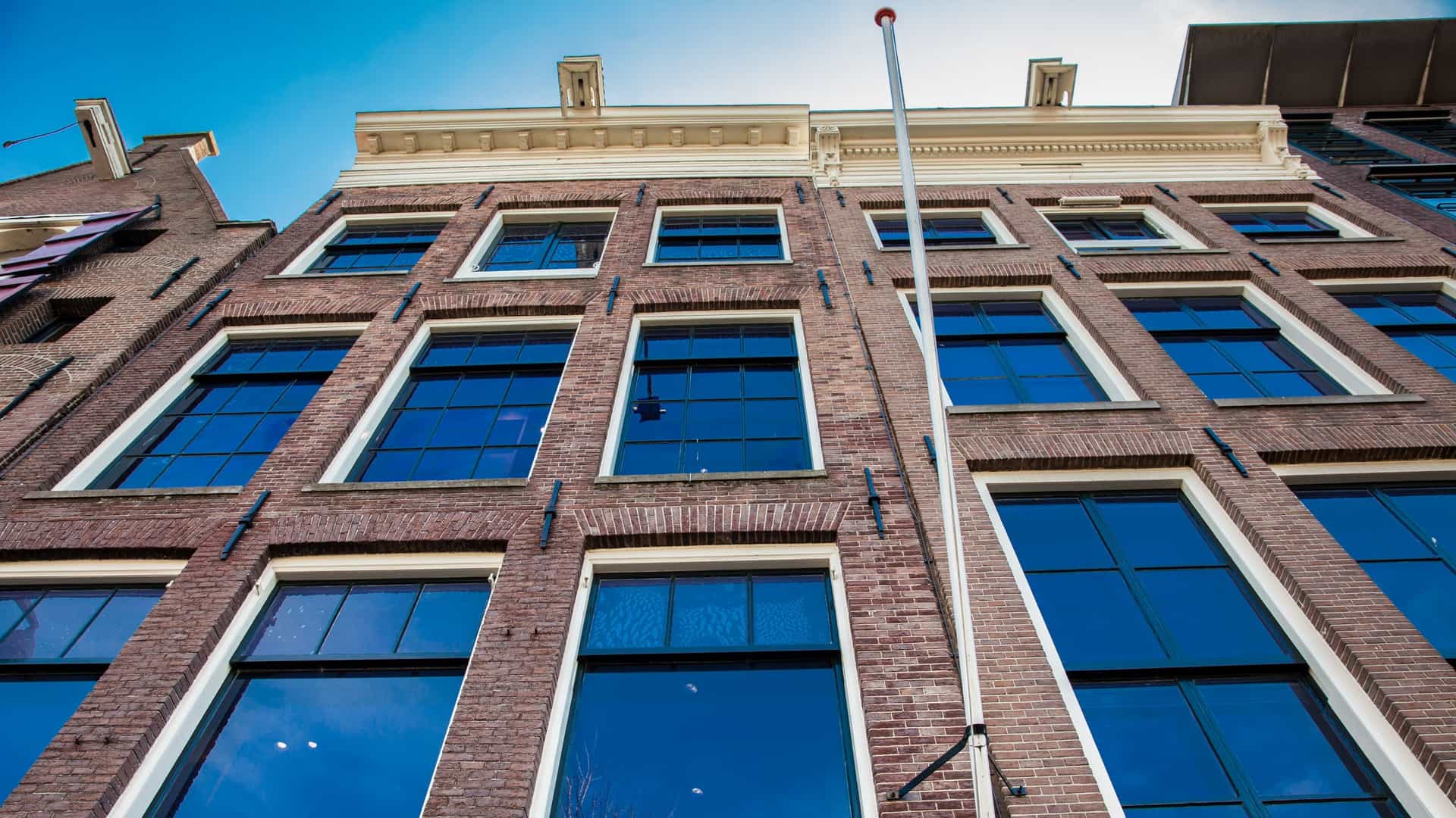 The narrow, historic canal-side façade of the Anne Frank House (Prinsengracht 263) in Amsterdam. The multi-story building features a traditional Dutch gabled roof, brickwork, and large windows, situated directly along the Prinsengracht canal in the city's old central district.