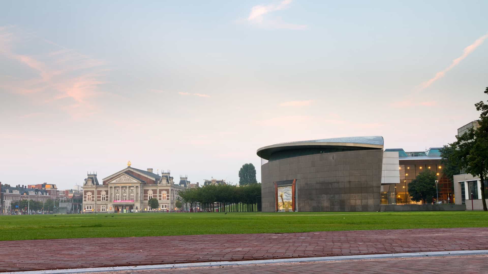 A view of the renewed, modern entrance to the Van Gogh Museum in Amsterdam. The structure is a large, contemporary, elliptical building featuring a transparent glass facade and roof, located on the Museumplein (Museum Square).
