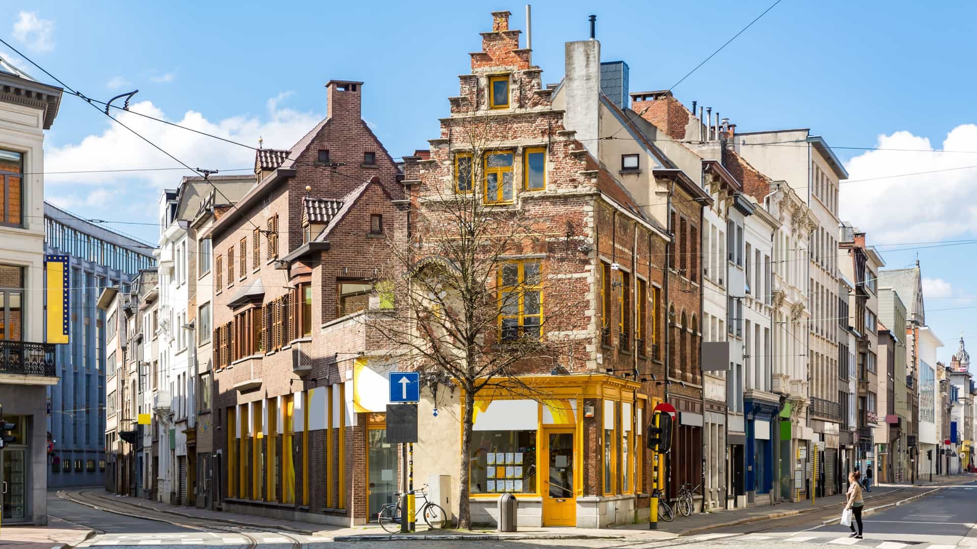 A lively cityscape of the Meir, the main shopping street in Antwerp, Belgium. The wide pedestrian boulevard is flanked by ornate, historic 18th and 19th-century buildings with modern storefronts, capturing a bustling urban scene.
