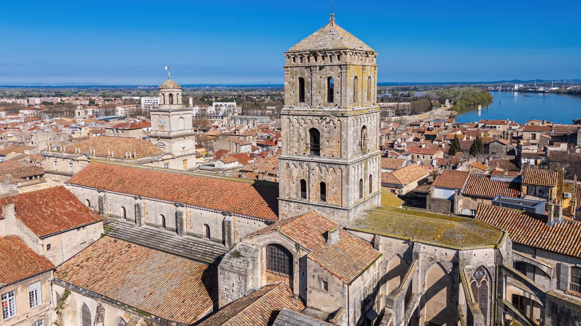 A view of the Cloister of the Church of St. Trophime in Arles, France, a UNESCO World Heritage site. The photo shows one of the covered galleries, characterized by a series of Romanesque and early Gothic arcades. The arches are supported by paired, carved marble columns with historiated capitals depicting biblical scenes.