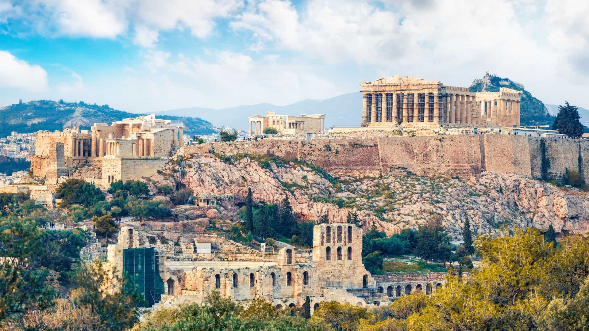 A captivating spring view of the Parthenon, an ancient temple on the Athenian Acropolis in Greece. The image captures the morning light on the historical structure, highlighting its classical columns and intricate details. The sky is a colorful backdrop, and the surrounding area appears to be in bloom with spring foliage.
