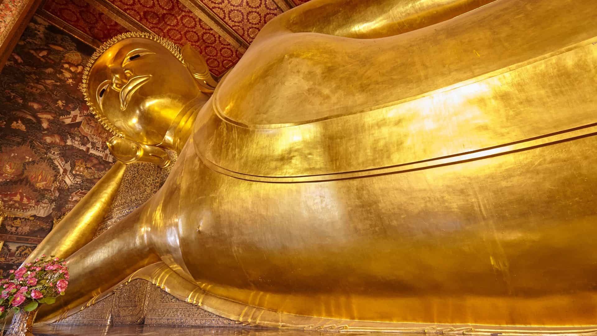 A close-up view of the giant, gold-leaf-covered Reclining Buddha statue at Wat Pho in Bangkok, Thailand, showing its serene expression and the intricate, mother-of-pearl inlaid soles of its feet which depict the 108 auspicious characteristics of the Buddha.