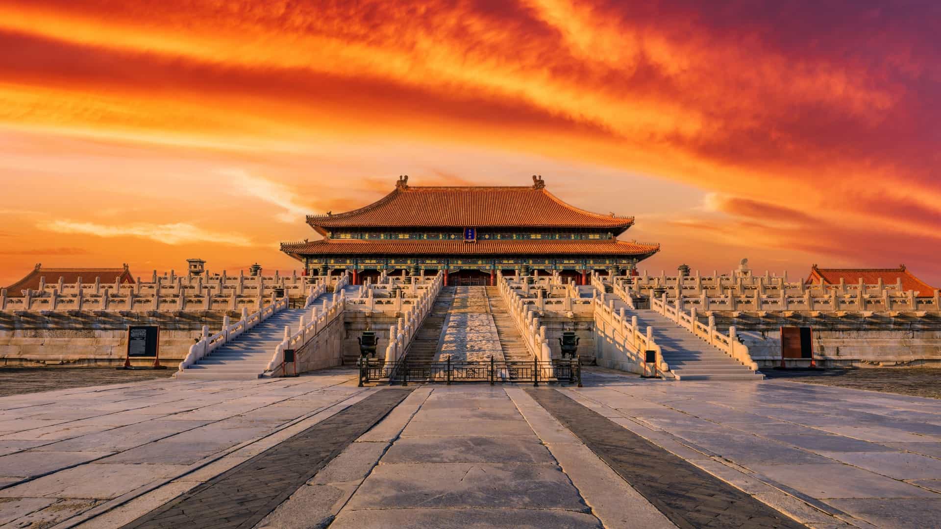 A majestic view of the Forbidden City in Beijing, China, with its traditional red and golden roofs, set against a vibrant and colorful sunset sky.