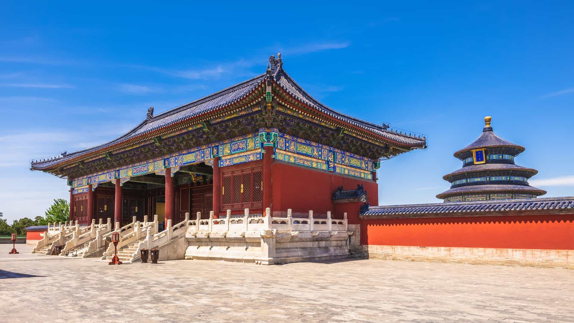 A clear, close up, low angle shot of the Hall of Prayer for Good Harvests, the main building of the Temple of Heaven complex in Beijing, China. The circular, three tiered building with its blue tiled roof and red pillars stands on a three level white marble base. The sky is bright and clear, highlighting the structure.