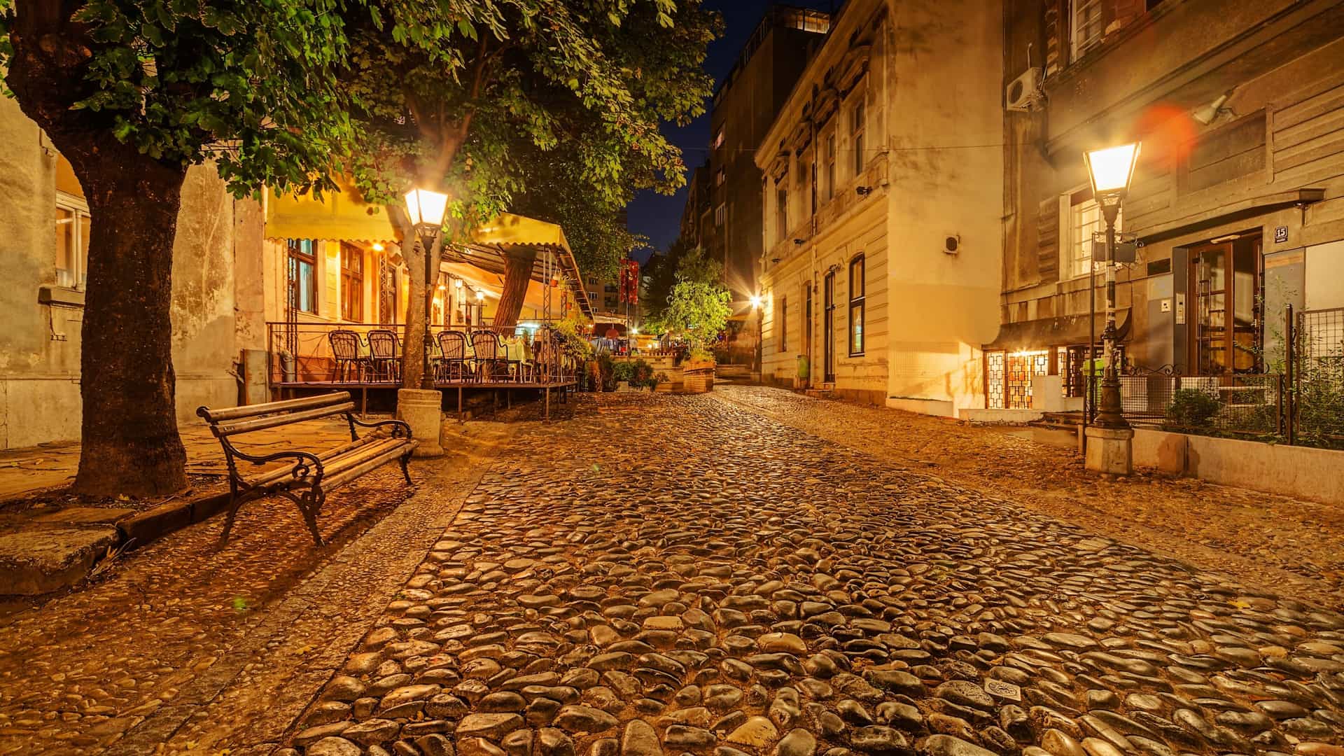 A vintage view of Skadarska Street (Skadarlija) in Belgrade, Serbia. The street is paved with cobblestones and lined with traditional buildings, giving it a classic, bohemian feel.
