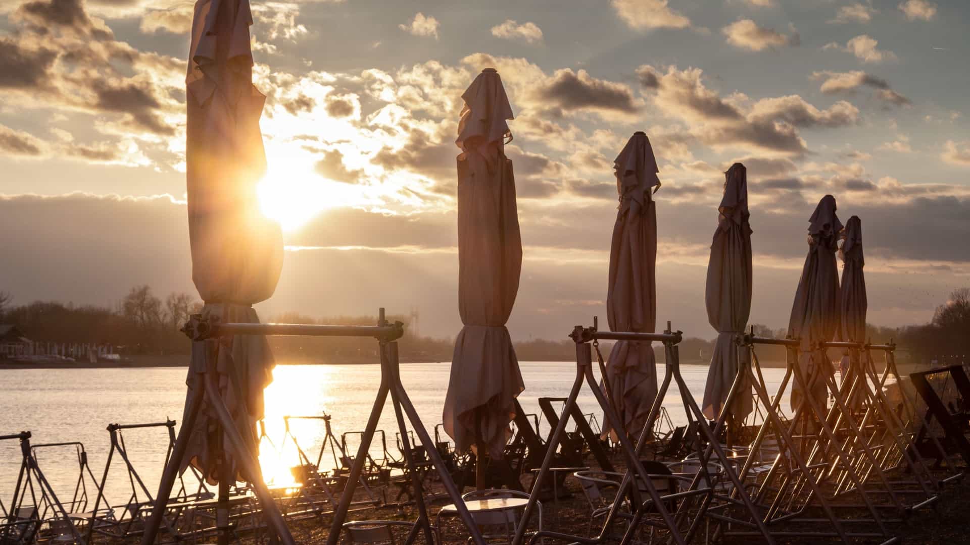 A close up, selective focus shot of empty cafe tables outdoors. The background is softly blurred with sunlight creating a bokeh effect, giving the image a warm, creative, and abstract atmosphere.