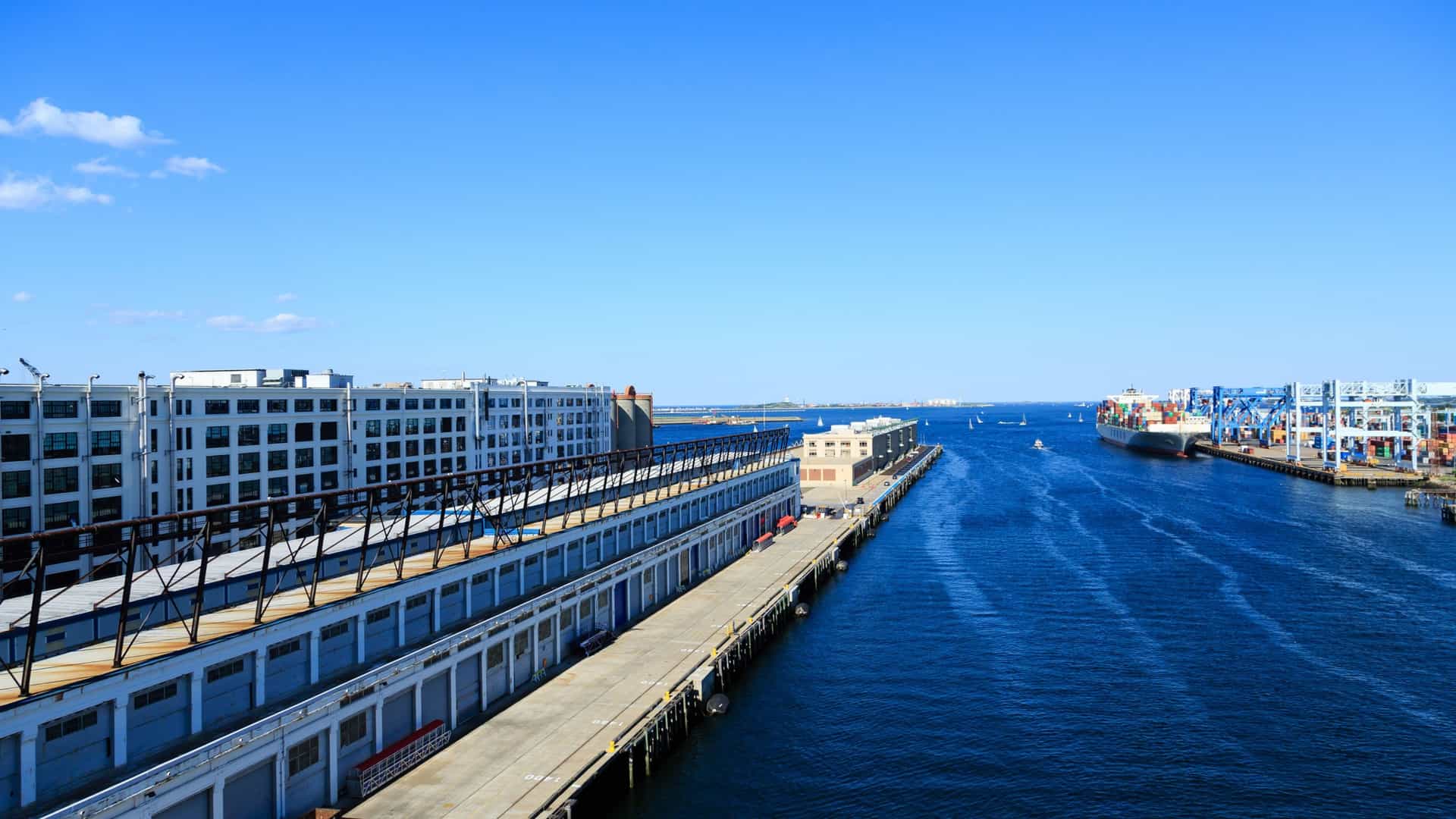 A bright, sunlit view of the Boston Harbor cruise channel with a large, white boat cutting through the blue water, creating a wake. The sky is clear, and the image captures the dynamic feeling of being on the water in the harbor.