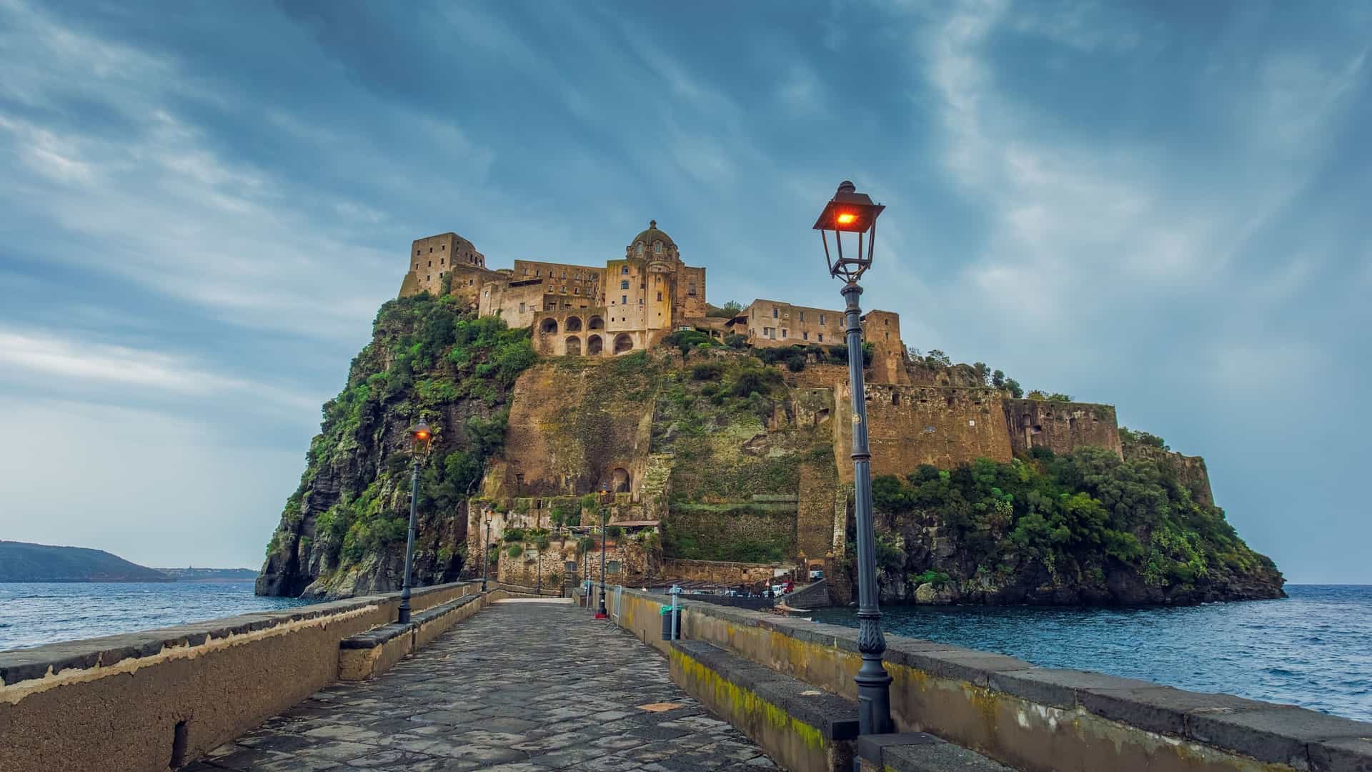 The Aragonese Castle (Castello Aragonese) on the island of Ischia, Italy, captured at dusk, featuring the medieval fortress perched on a rocky islet in the Mediterranean Sea.