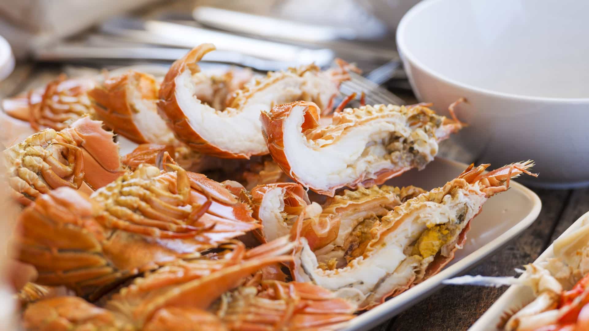 A large seafood platter for an outdoor lunch, featuring a mix of grilled crustacea such as bright pink Moreton Bay Bugs, shrimp, and other shellfish.