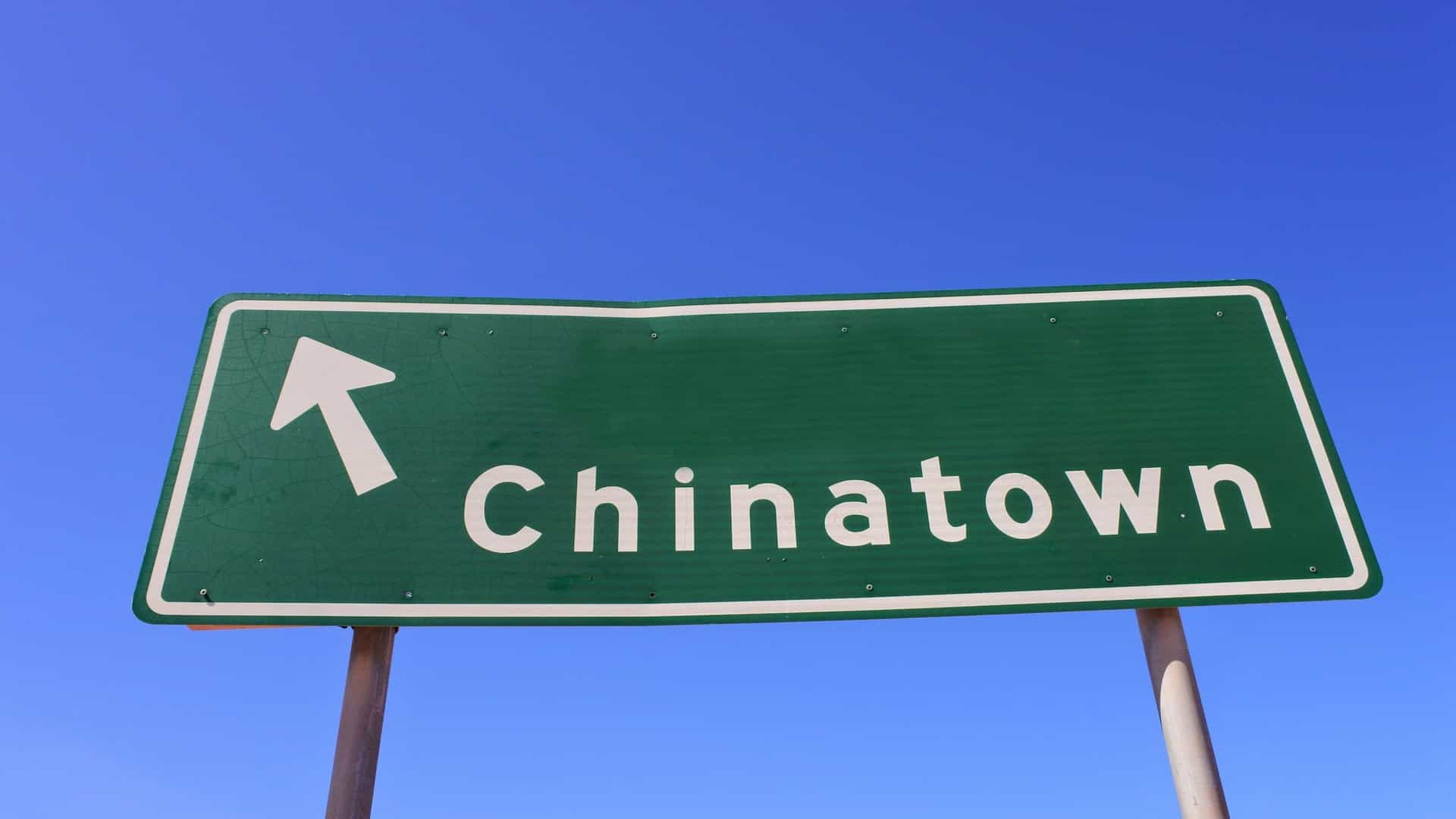 A close-up of a green directional street sign with a yellow border, featuring a white arrow pointing to the right and the text "Chinatown," indicating the location of the historically significant Chinese quarter in Broome, Western Australia.