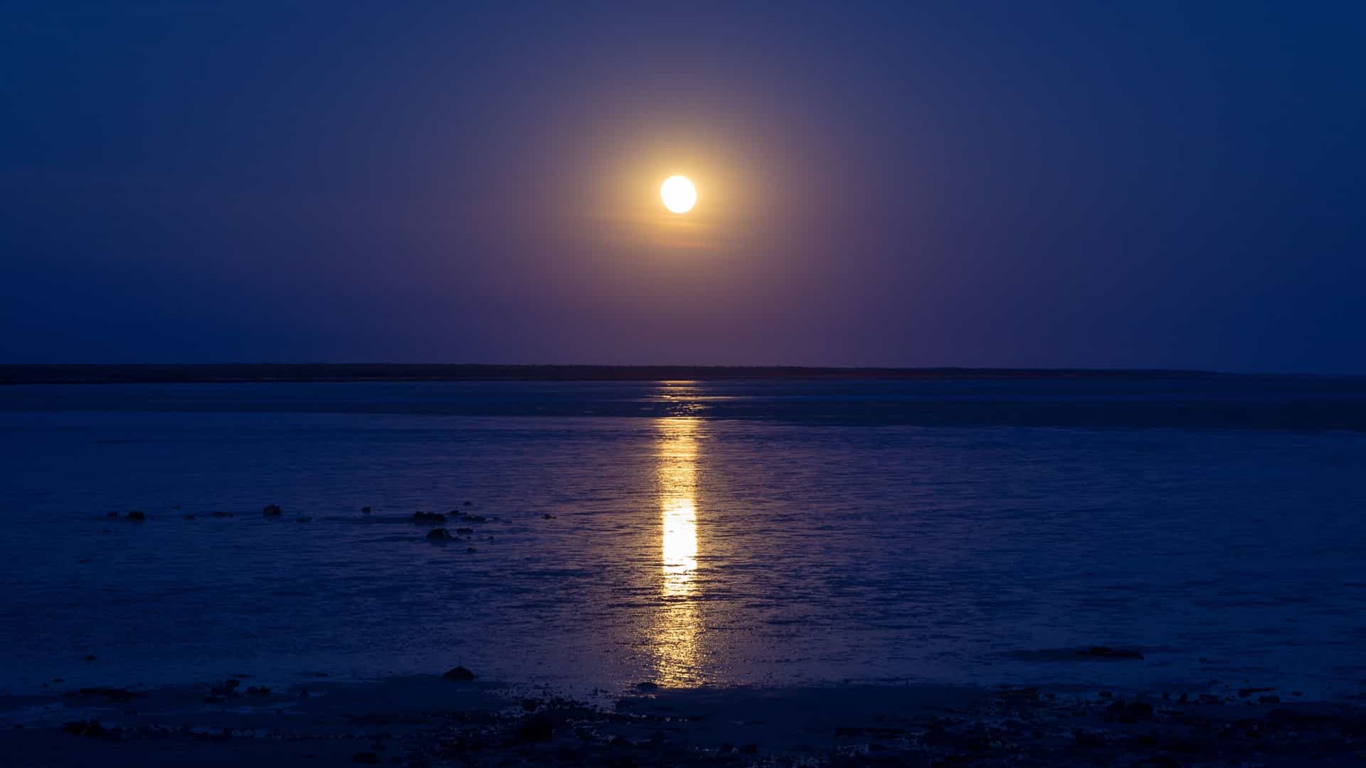 The natural phenomenon known as the "Staircase to the Moon" over Roebuck Bay in Broome, Western Australia, with the light of a rising full moon reflecting across the exposed, rippled tidal flats to create the illusion of a shimmering staircase.