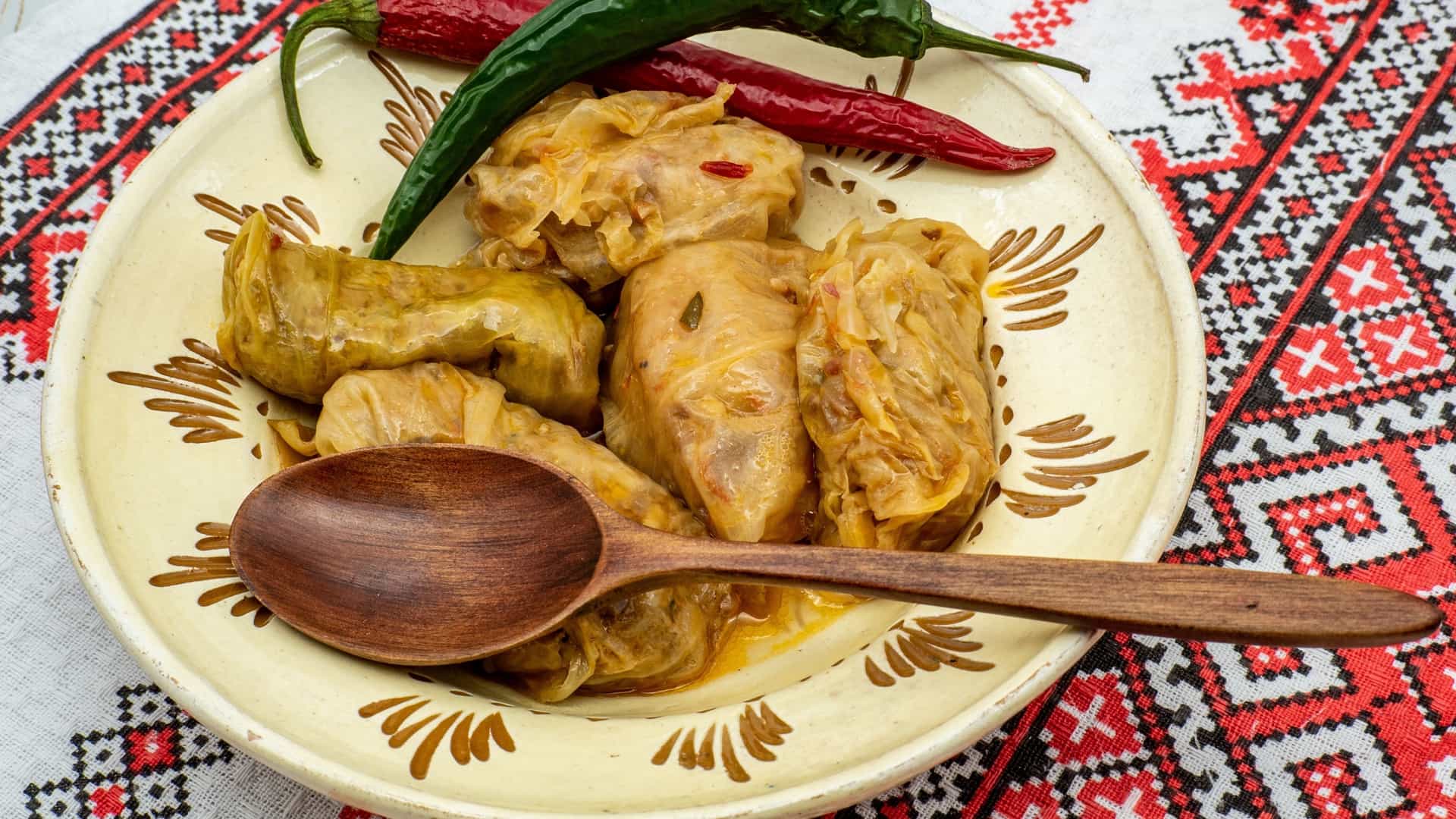 A close up view of traditional Romanian cabbage rolls, known as sarmale, served in a clay pot, garnished with a dollop of sour cream (smântână) and pieces of smoked bacon or ham, ready to be eaten.