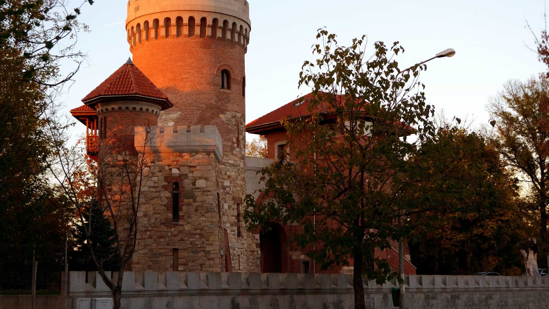 The Vlad Tepes Castle (or Vlad the Impaler's Tower), a medieval style fortress replica located in Carol Park, Bucharest, Romania, is dramatically illuminated by the warm, glowing light of the sunset.