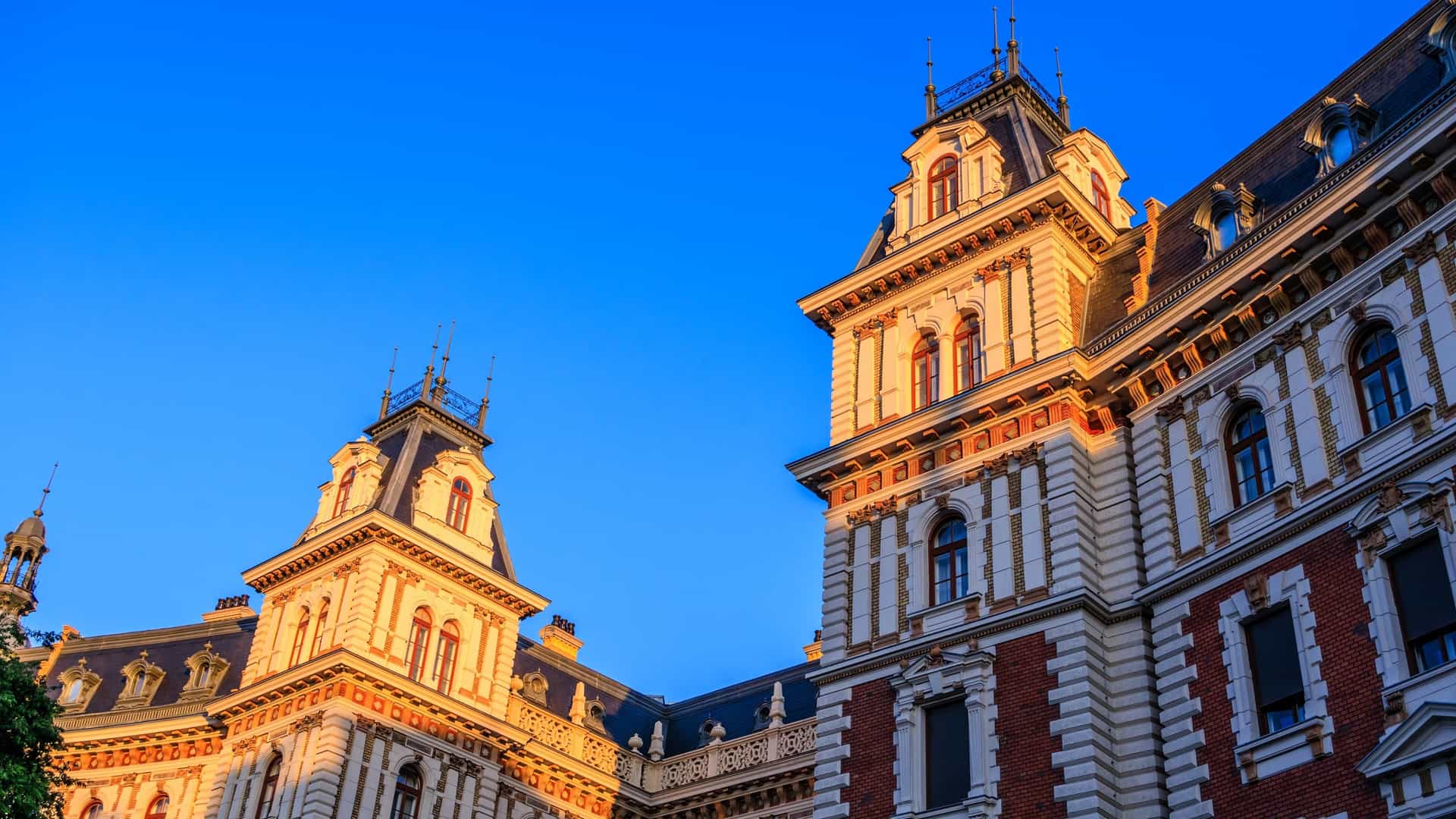 A close up view of the facade of a luxurious Neo Renaissance mansion on Andrássy Avenue in Budapest, Hungary, a UNESCO World Heritage site. The vintage building features ornate architectural details, including sculptural decorations, columns, and a large, intricately carved wooden door. The building's age and historical elegance are highlighted.