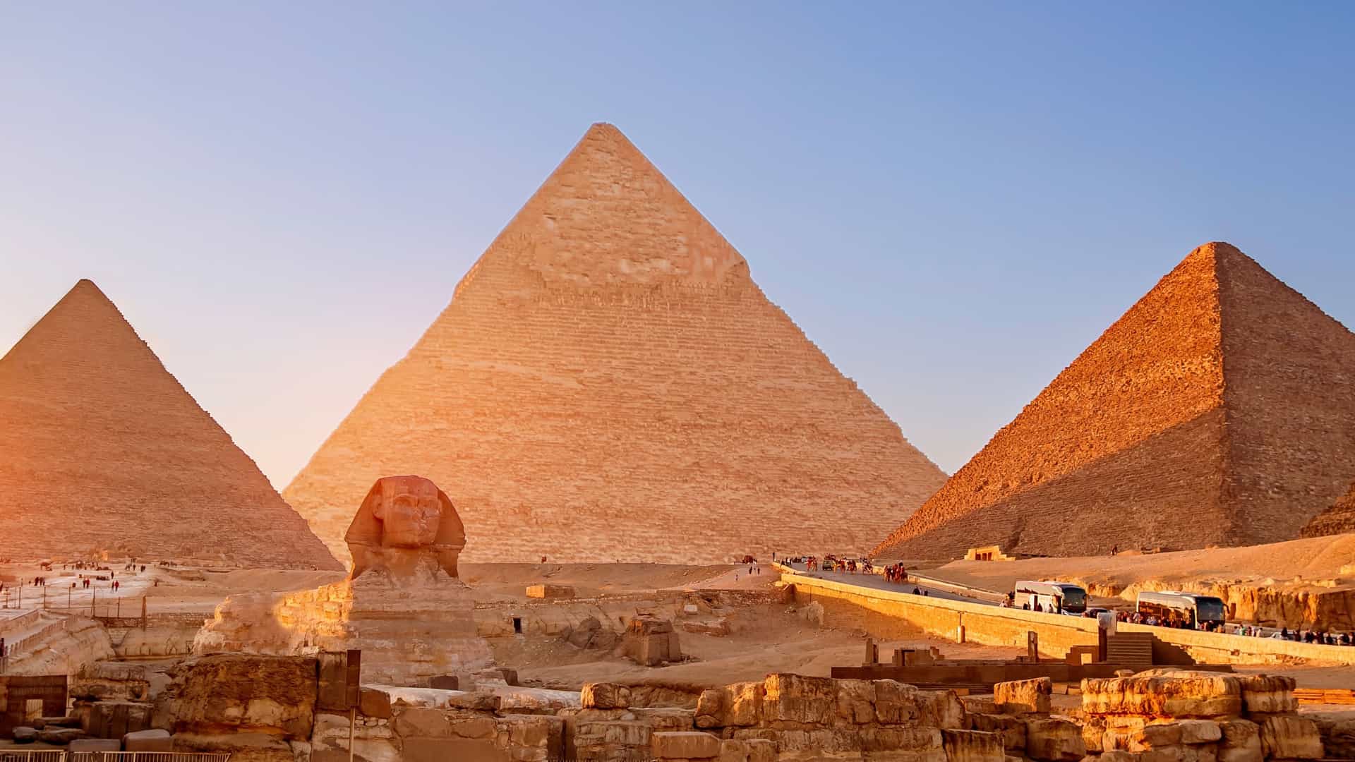 A wide banner view of the Great Sphinx of Giza with the Pyramids of Giza in the background, set against a clear blue sky.