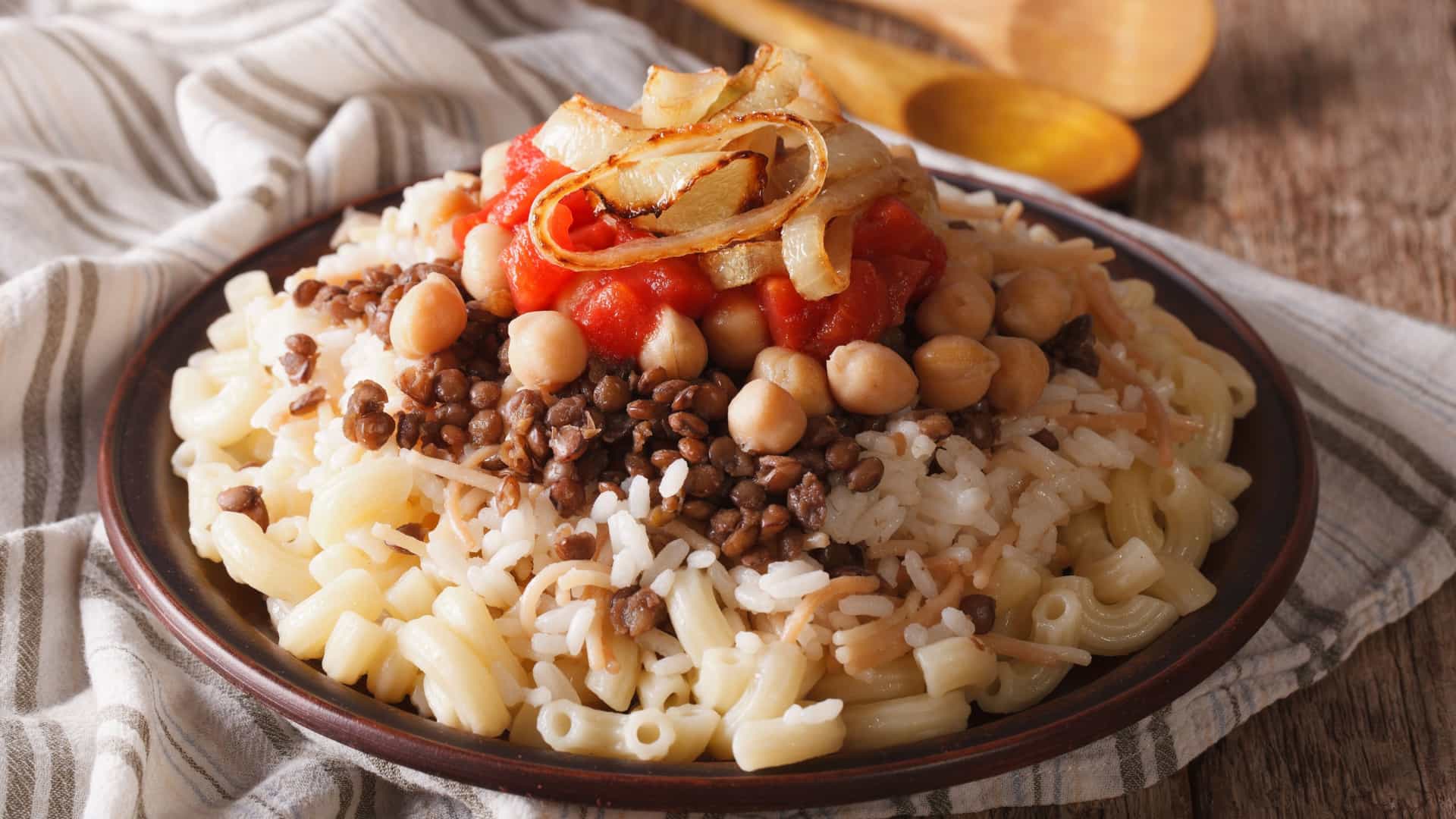 A close up of a bowl of Kushari, the traditional Egyptian national dish, featuring a flavorful mix of rice, pasta, lentils, chickpeas, and crispy fried onions.