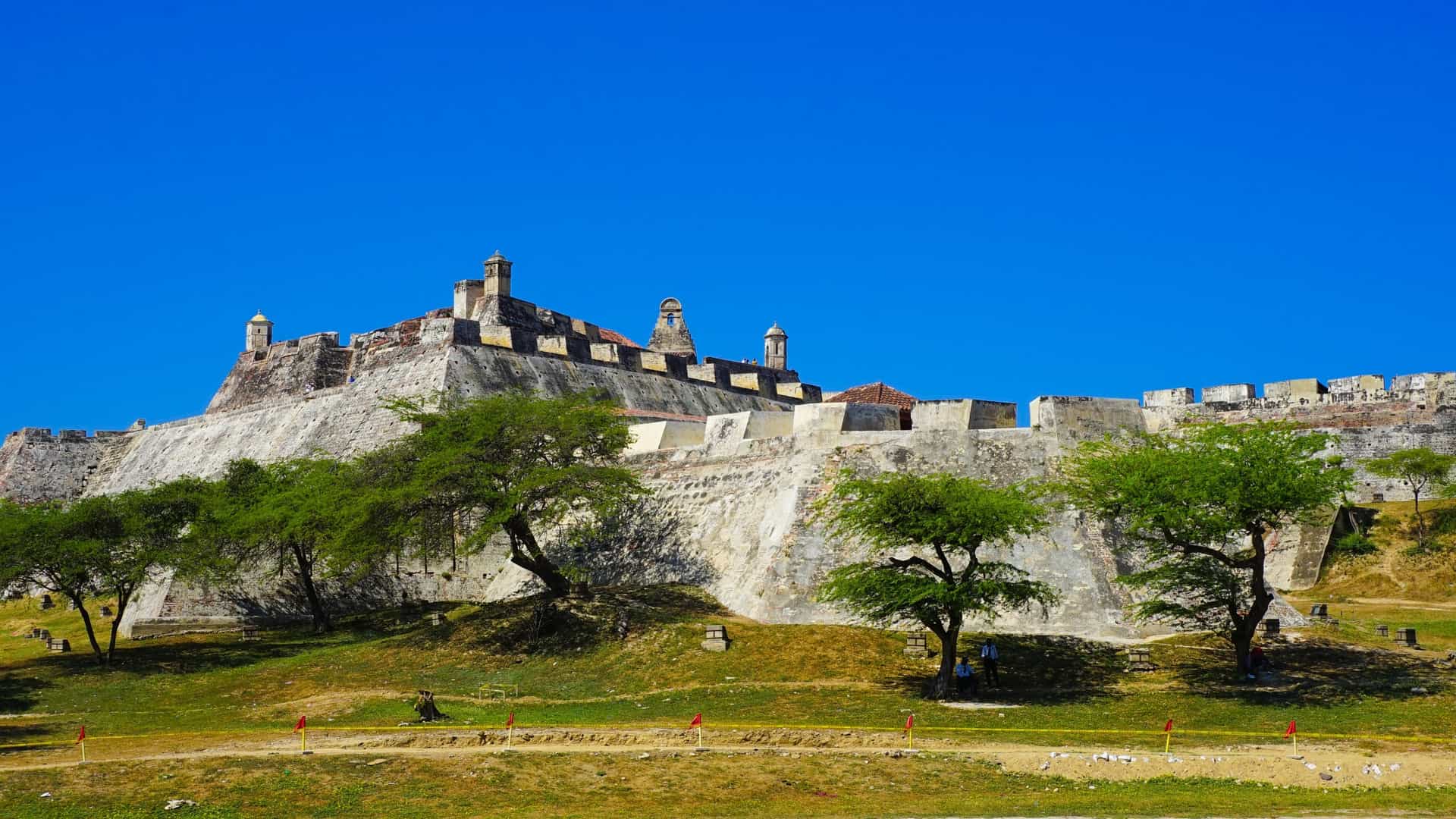A view of the Castillo San Felipe de Barajas fortress in Cartagena, Colombia. The image shows the vast, stone built fortress with its intricate system of walls and battlements, situated on a hill with the city visible in the background.