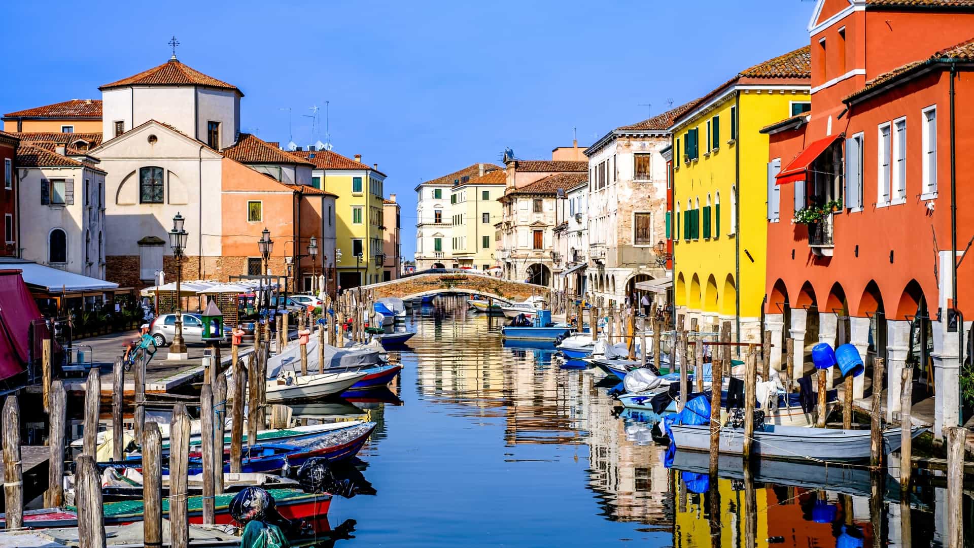 A picturesque view of the famous old town of Chioggia, Italy, showcasing colorful, densely packed buildings lining a canal where boats are moored, reflecting the town's Venetian heritage.