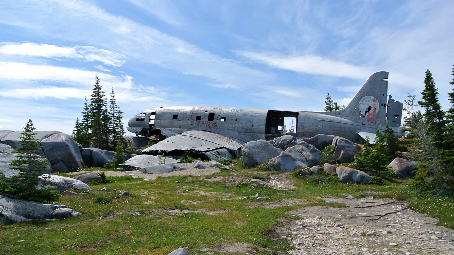 The wreckage of the Curtiss C 46 Commando cargo plane, known as "Miss Piggy," rests on a rocky, snow dusted tundra landscape near Churchill, Manitoba. The plane, which crashed in 1979 and is a local landmark, features a modern mural painted across its fuselage.