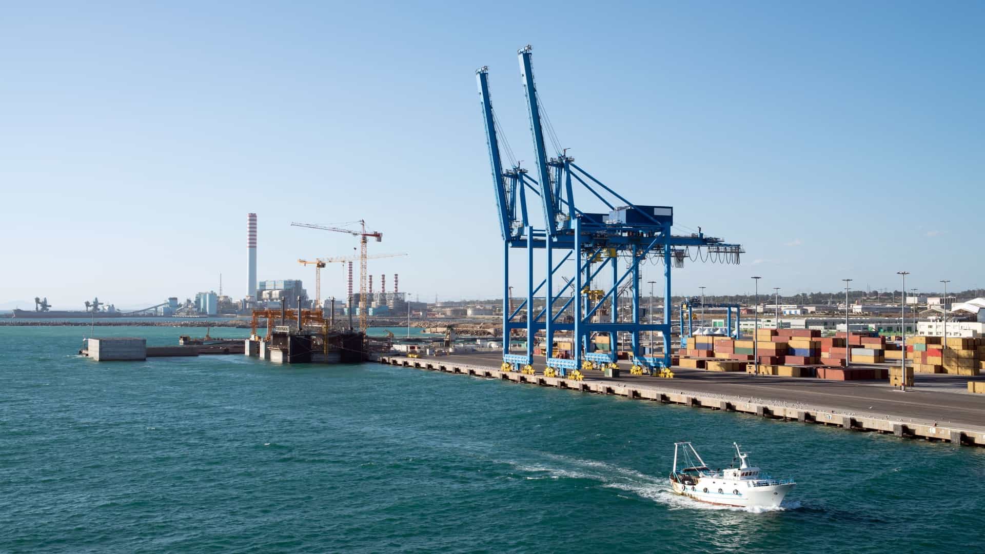 An aerial or high-angle view of the Port of Civitavecchia (Porto di Civitavecchia), Italy, showing the large cruise ships and ferries docked in the commercial harbor next to the historic stone breakwaters and the city's waterfront buildings.