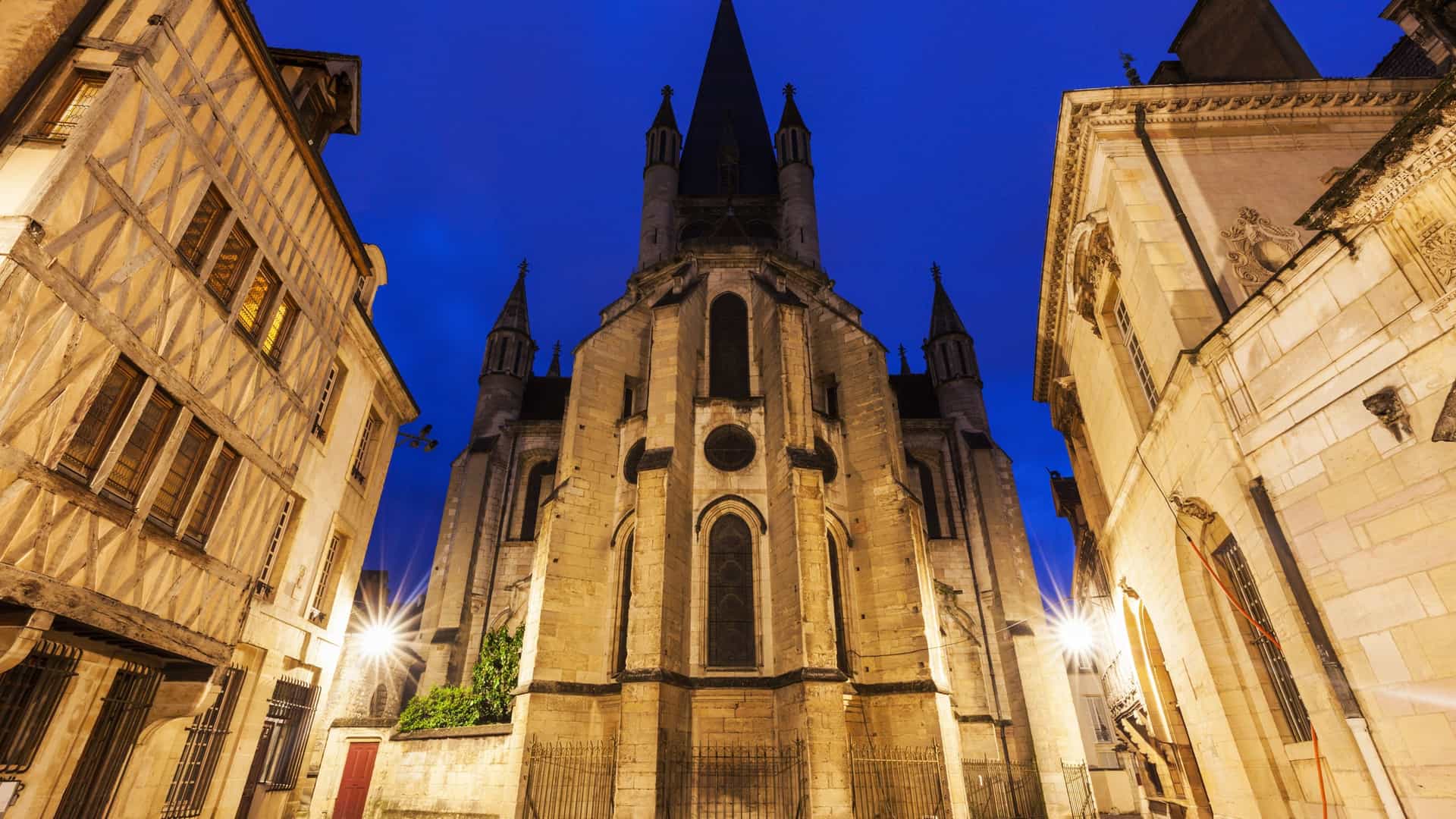 The ornate facade of the Church of Notre Dame in Dijon, France. The Gothic architecture is defined by three tiers of arcades with slender columns and numerous carved figures, with the iconic Jacquemart clock visible on the top of the tower.