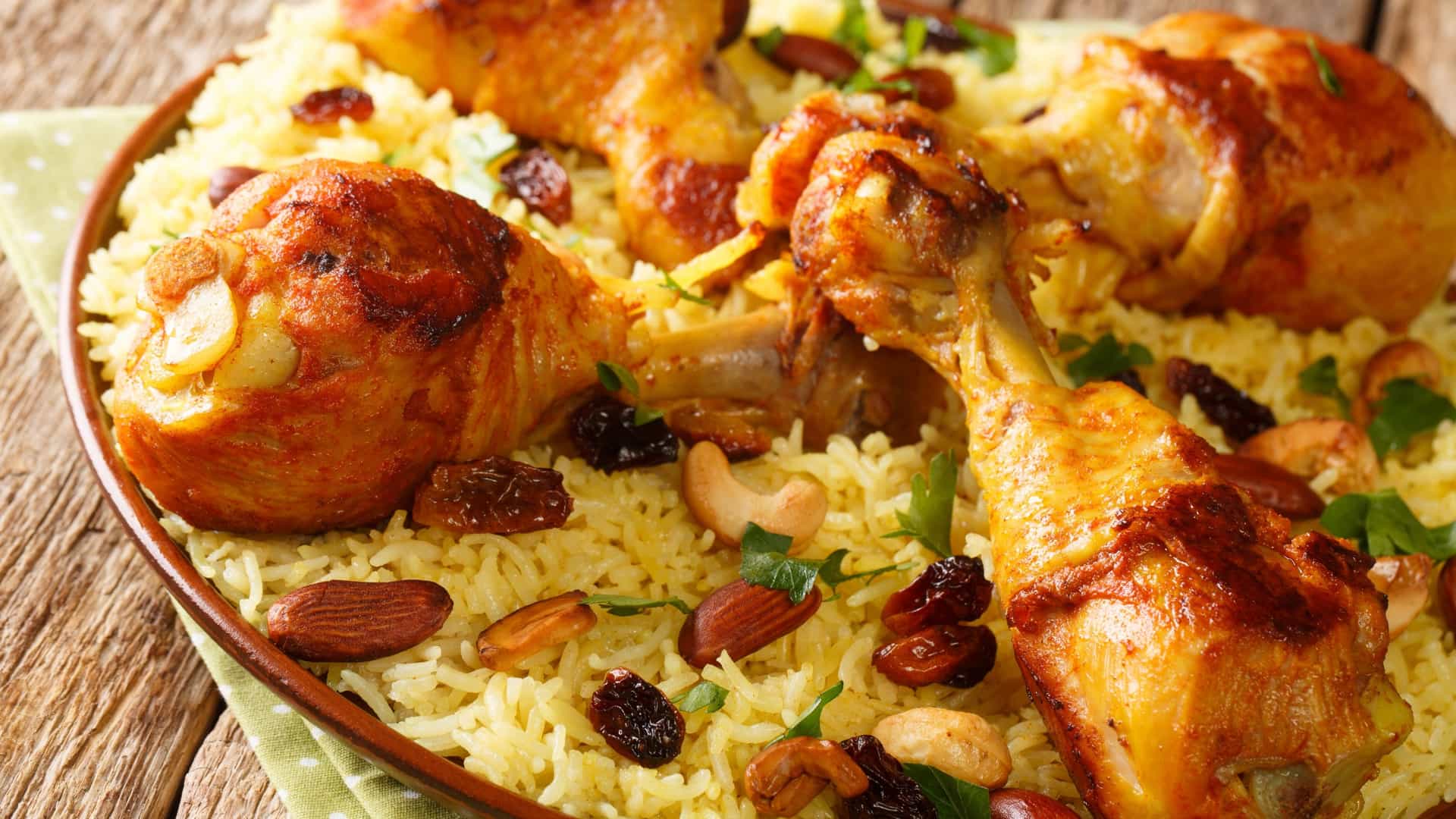 A dish of Arabic Chicken Majboos, featuring a bed of spiced, saffron colored basmati rice topped with a roasted or fried chicken piece. The dish is typically garnished with nuts (like slivered almonds or pine nuts) and raisins, and is a popular traditional meal from the Arabian Gulf region.