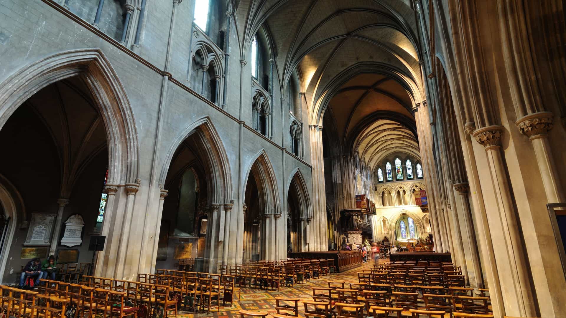 A photograph of St. Patrick's Cathedral in Dublin, Ireland. The cathedral is a large, ornate building constructed in the Gothic architectural style. The image likely shows the exterior of the cathedral, with its prominent spire and intricate stonework. It may also show parts of the surrounding park and visitors.