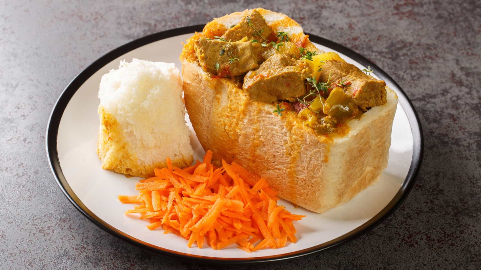 A street vendor's stall featuring a selection of traditional African bread-based street food, possibly in Durban, South Africa. The image shows freshly made, hollowed-out loaves of bread (known as Bunny Chow in Durban) ready to be filled.
