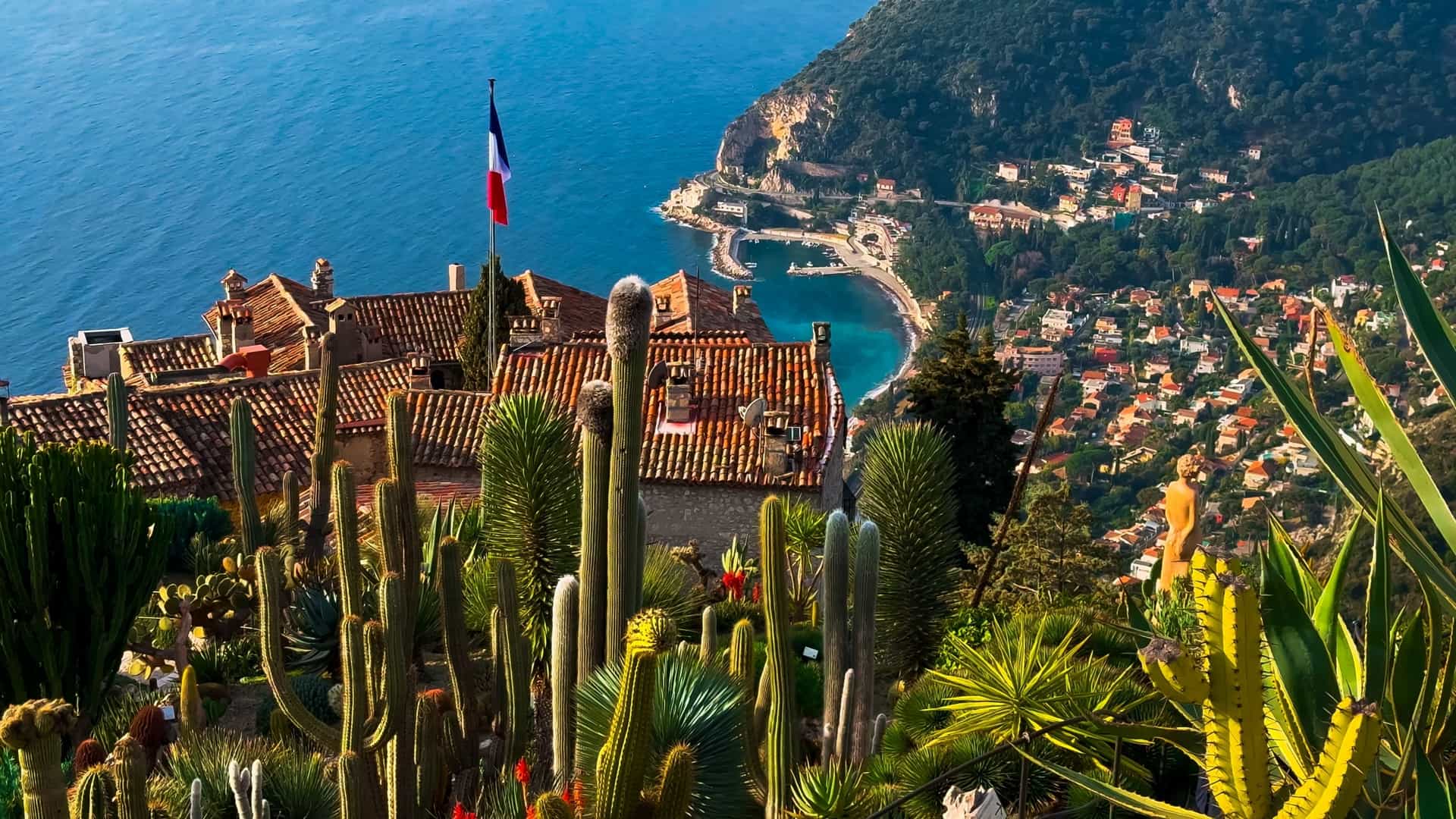 A high angle view of the Exotic Garden of Èze, located in the French hilltop village of Èze. The garden features a variety of cacti and other succulents growing among the ruins of a medieval fortress, with a panoramic view of the Mediterranean Sea and the coastline below.