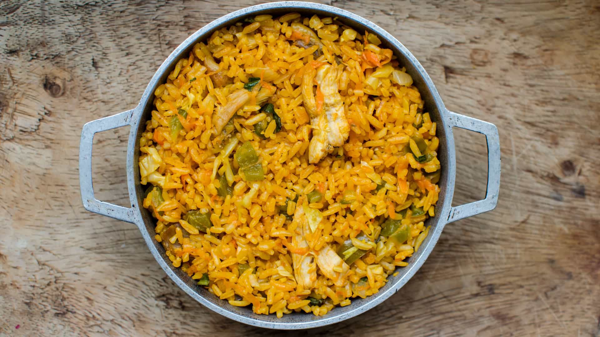 A close-up shot of a serving of traditional Panamanian Arroz con Pollo (Rice with Chicken). The rice is a warm, orange-yellow color, flecked with pieces of shredded chicken, peas, carrots, olives, and pimientos. The dish is typically served in a bowl, showcasing the moist, seasoned rice that is a quintessential comfort food in Panamanian cuisine.