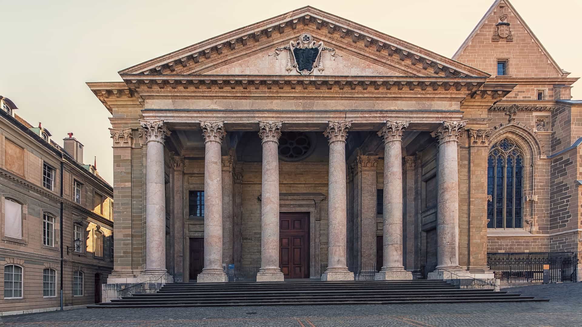 A frontal view of the Neoclassical facade of St. Pierre Cathedral in Geneva, Switzerland, featuring a grand portico with six tall Corinthian columns supporting a triangular pediment. The view captures the stark contrast between this 18th-century entrance and the older, darker, Romanesque and Gothic towers flanking it, under a clear sky, highlighting the cathedral's historical layers.