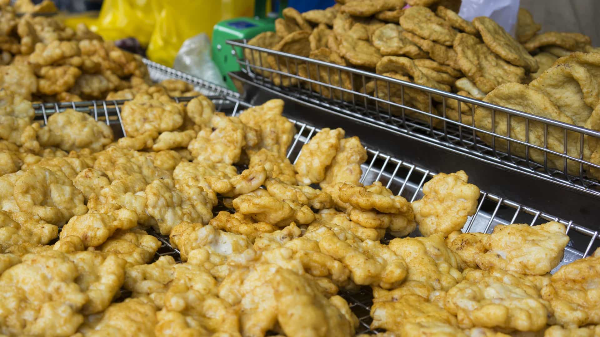 A close up, top down view of a platter of "chả mực," a famous Vietnamese dish of fried ground squid from Ha Long Bay. The dish consists of several golden brown, irregularly shaped patties arranged on a dark plate, with a small dish of a reddish dipping sauce on the side.