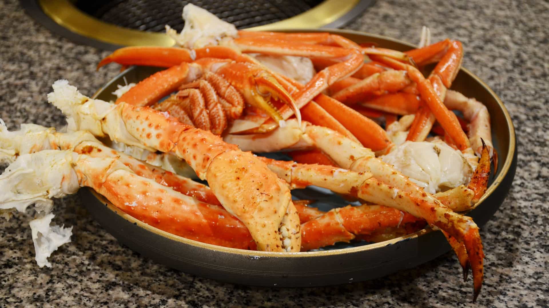 A close-up photograph of steamed Alaskan King Crab legs served on a plate, garnished with a wedge of lemon and a cup of melted butter for dipping. The vibrant red-orange shells and the rich texture of the crab meat highlight the gourmet seafood delicacy.