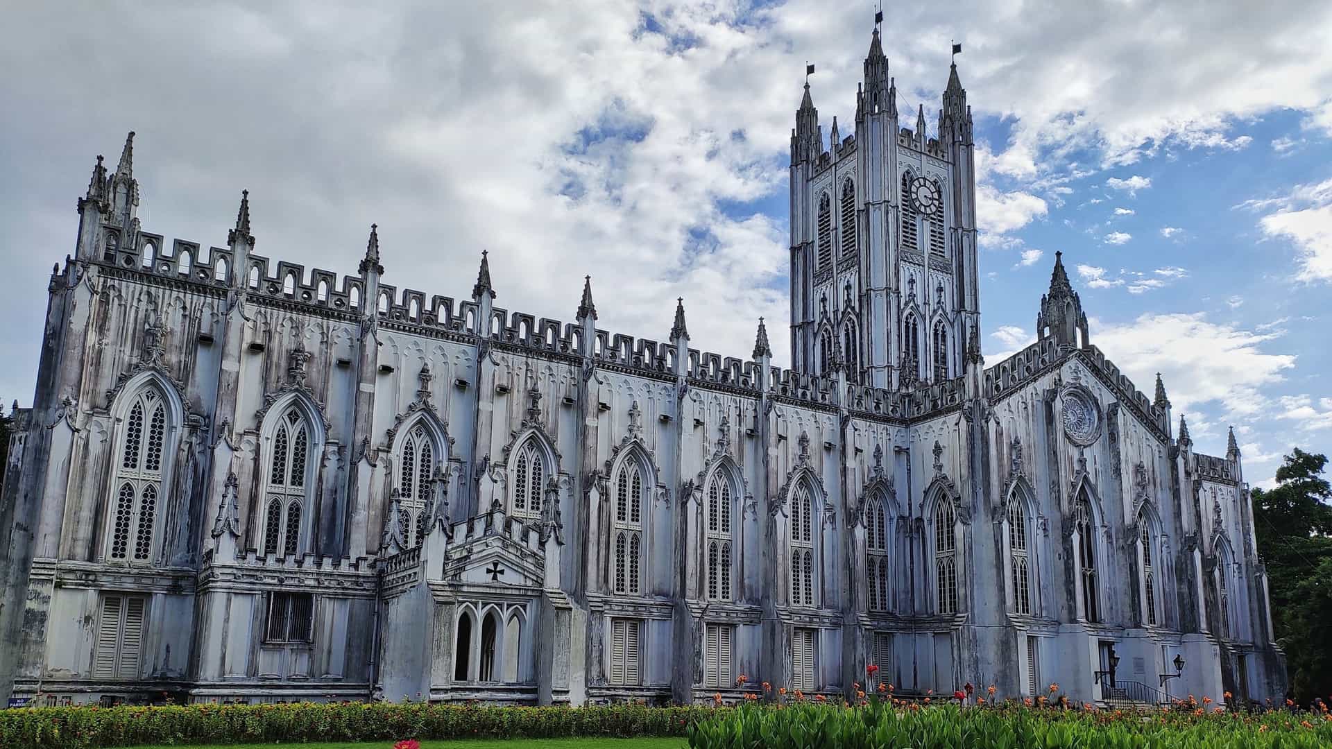 The magnificent white Gothic Revival architecture of St. Paul's Cathedral in Kolkata, India. The image captures the church's tall spire and detailed facade from an exterior view, set against a bright sky.