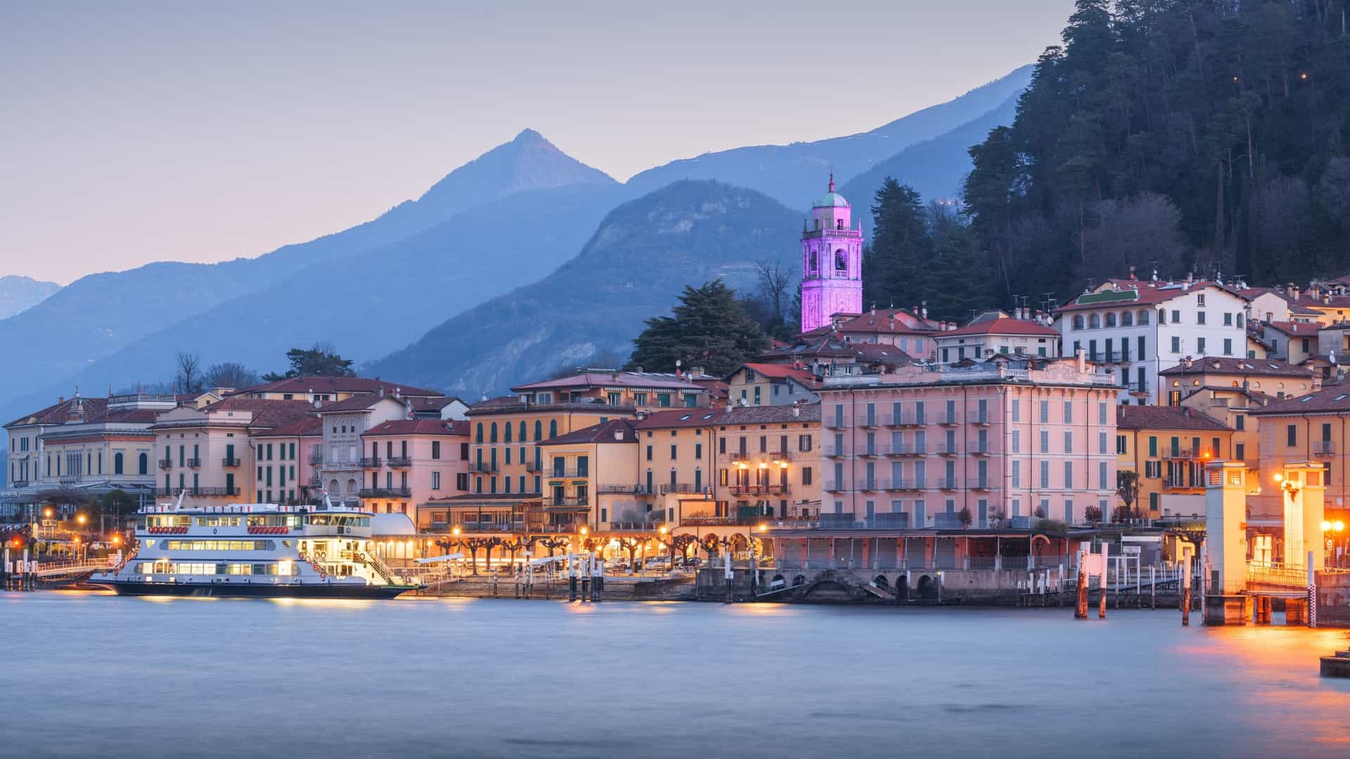 The town of Bellagio, Italy, on Lake Como, captured at dawn with lights reflecting on the still water.
