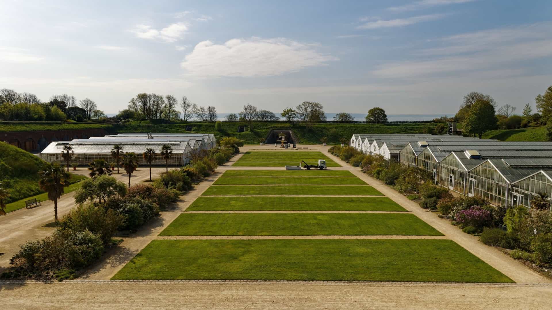 An elevated, panoramic view of The Hanging Gardens (Les Jardins Suspendus) in Le Havre, France. This 17-hectare botanical garden is set within the ramparts of the old 19th-century Fort de Sainte-Adresse. The image typically captures the fort's historic walls and themed gardens (often featuring flora from around the world), offering a stunning view that looks out over the lower city, the port, the Seine estuary, and the English Channel.