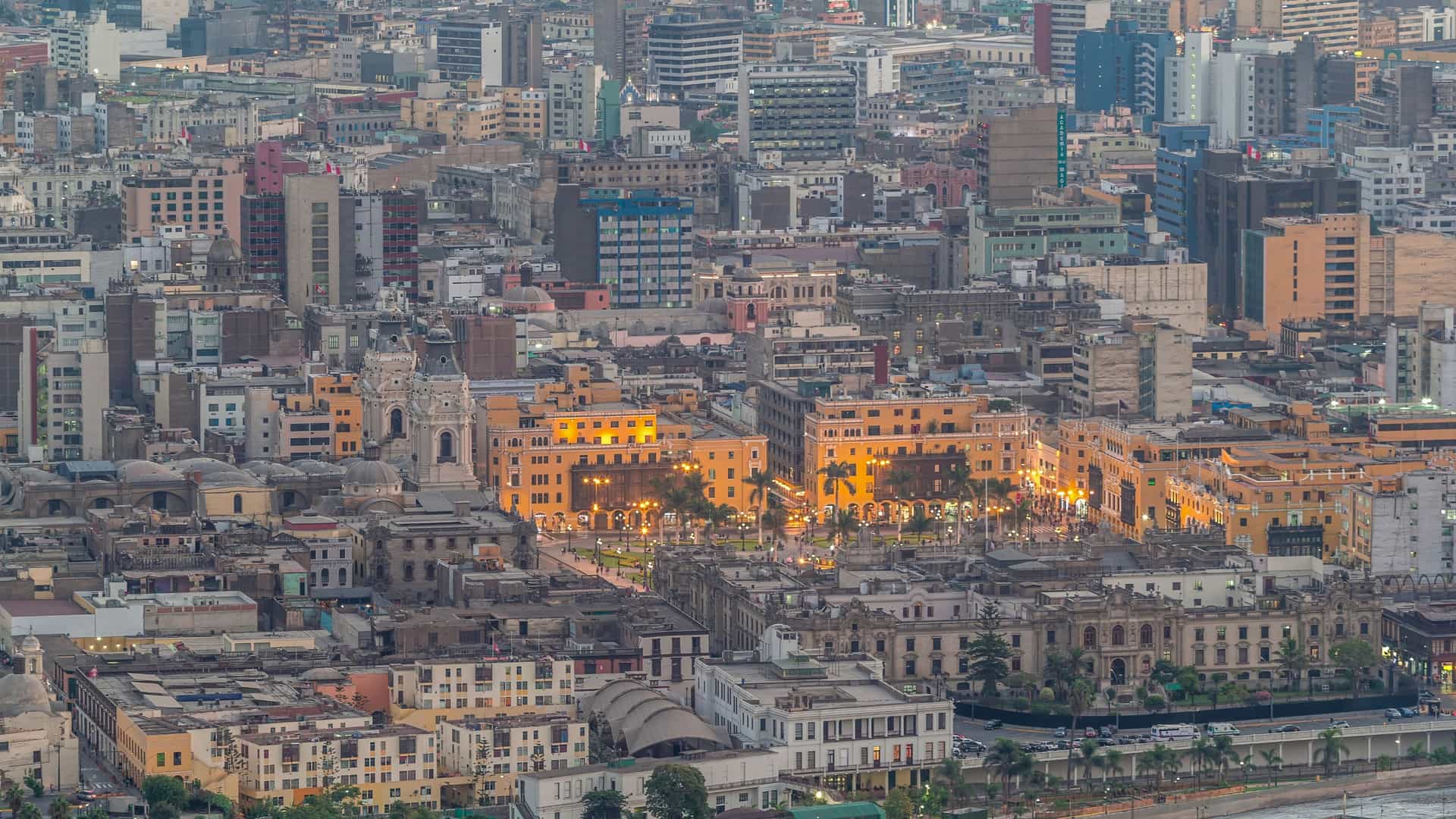 An aerial, top down view of the main square in Lima, Peru, also known as Plaza de Armas. The image, taken on a sunny day, shows the historic square surrounded by key landmarks, including the Lima Cathedral and the San Francisco Church, with people visible in the square below.