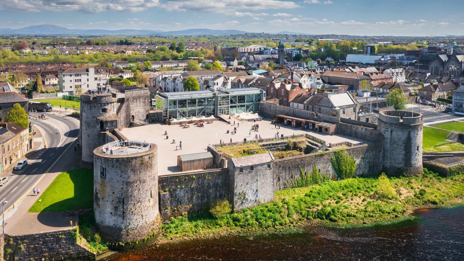 The historic King John's Castle, a medieval 13th-century fortress, is situated on King's Island in Limerick, Ireland. Its stone curtain walls and cylindrical corner towers overlook the tranquil waters of the River Shannon, creating a striking ancient landmark.