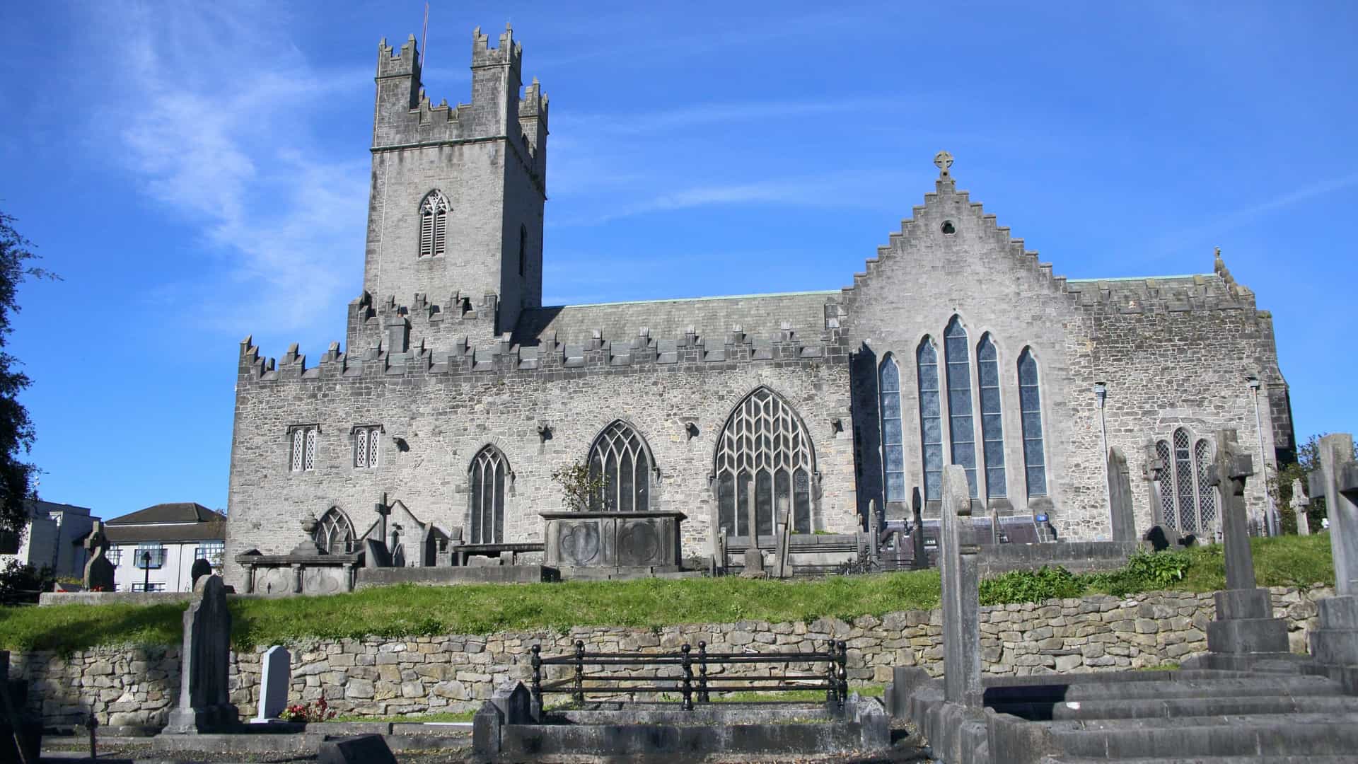 An exterior view of Saint Mary's Cathedral in Limerick, Ireland. The medieval stone cathedral, which is the oldest building in continuous use in the city, features a tall tower and is surrounded by its historic grounds and trees.