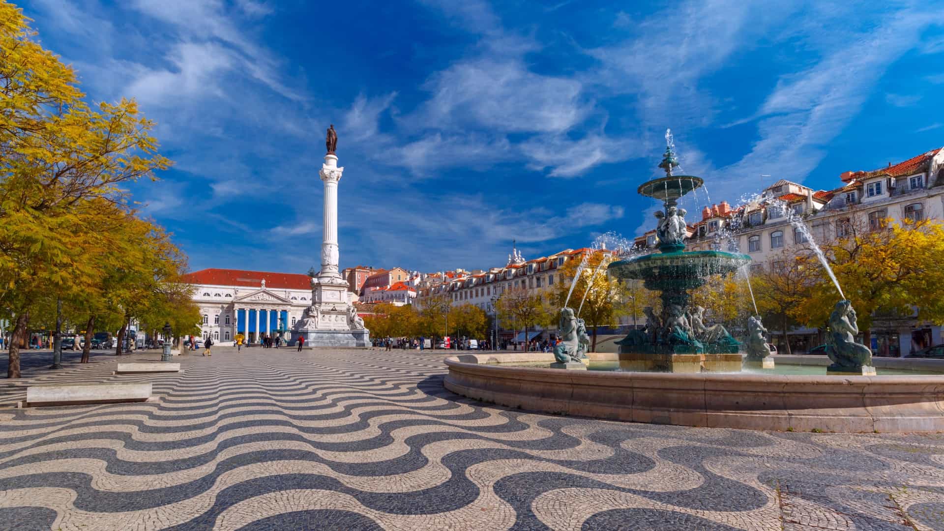 A close up view of the iconic black and white wavy cobblestone pavement, known as "calçada portuguesa," in Rossio Square (Praça de D. Pedro IV) in Lisbon, Portugal. The wavy pattern, which is also referred to as "Mar Largo" or "Wide Sea," creates a striking optical illusion, with the fountain and monument in the background slightly out of focus.