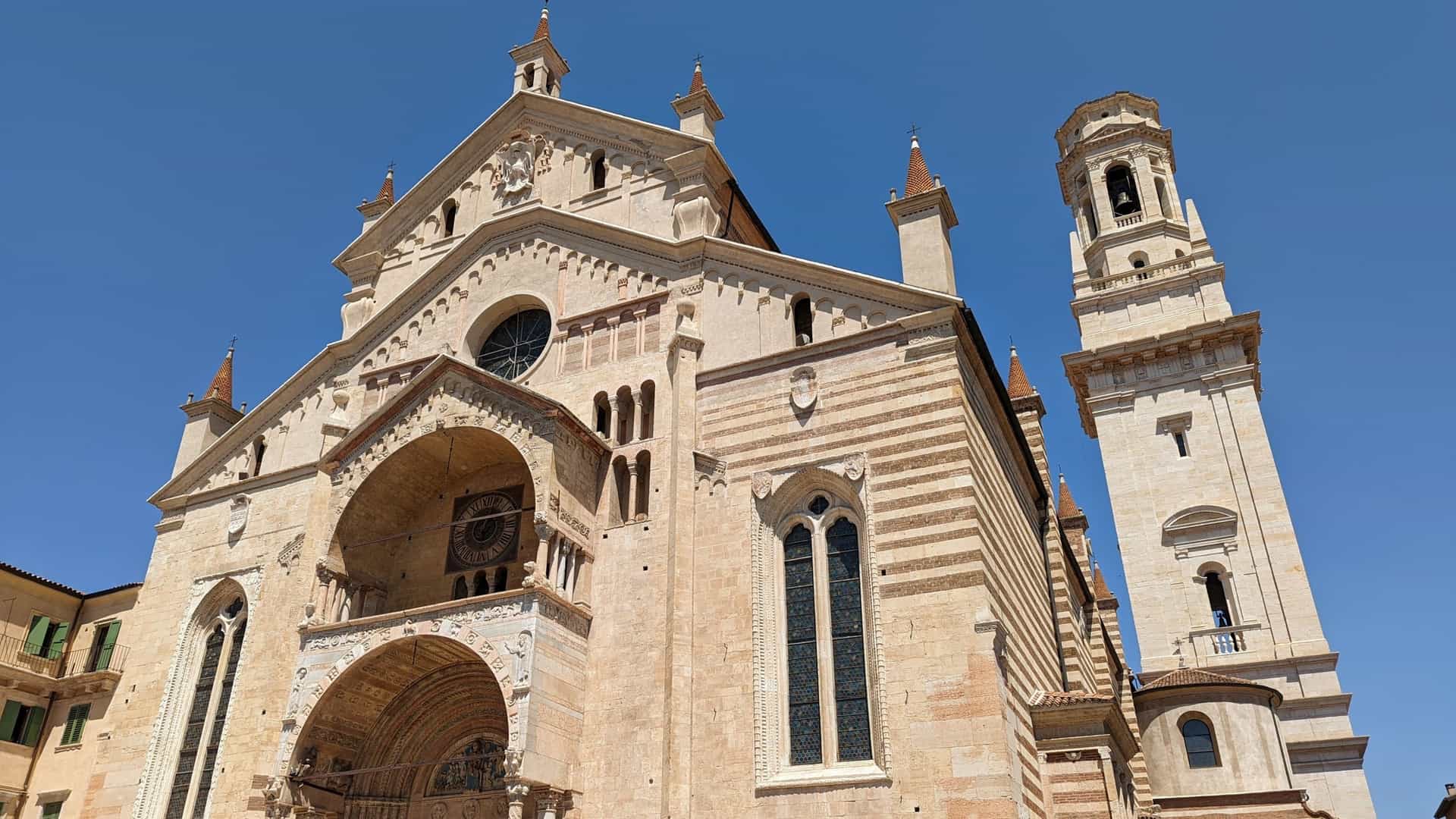 An exterior view of the Complesso del Duomo di Verona (Verona Cathedral) in Verona, Italy, showcasing the Romanesque style of the main entrance, which features a prominent portico and a central rose window above.