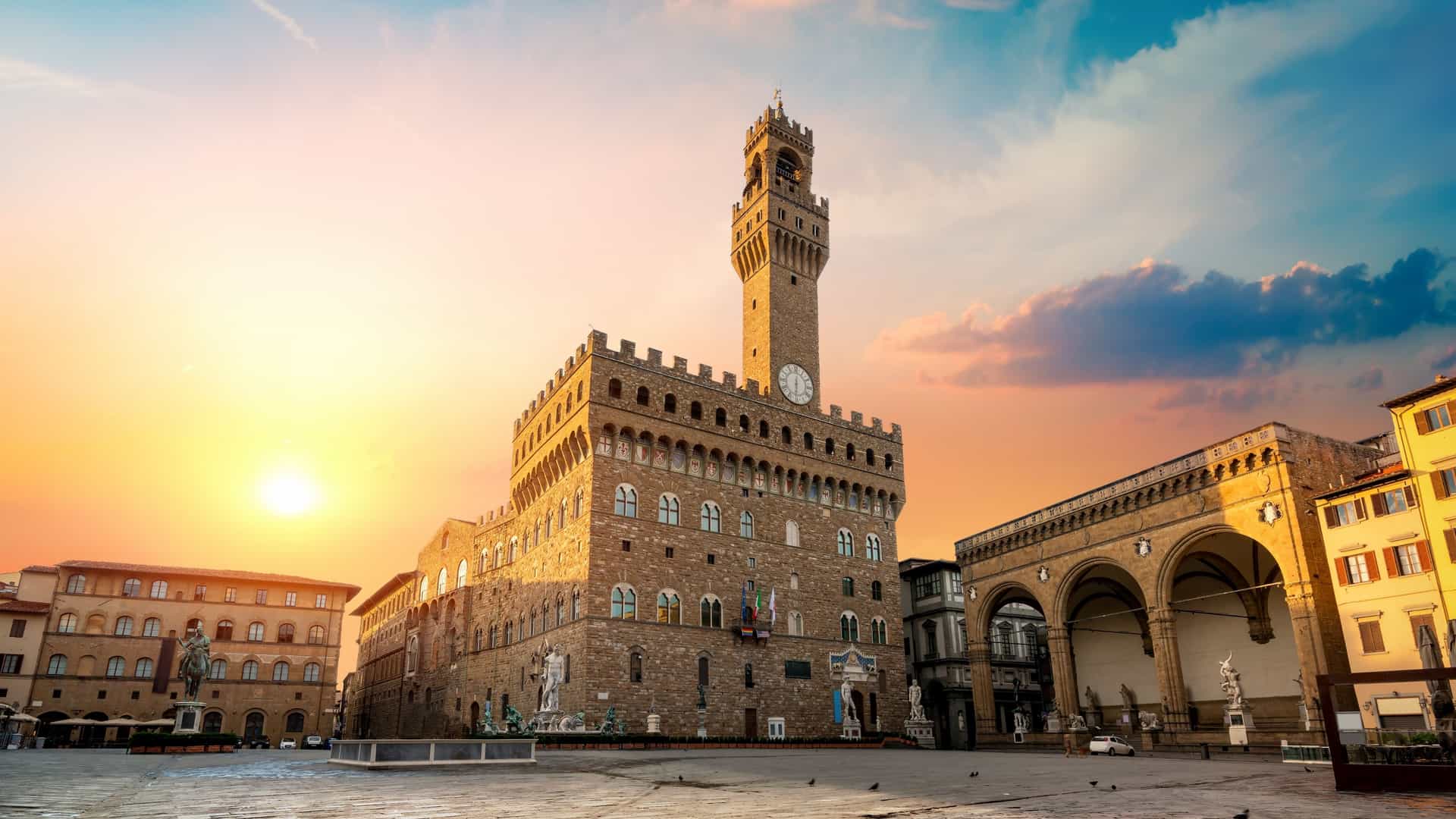 A view of Piazza della Signoria in Florence, Italy, during sunrise. The photograph captures the famous statues in the square's Loggia dei Lanzi, including a prominent view of the equestrian statue of Cosimo I and the Palazzo Vecchio in the background.