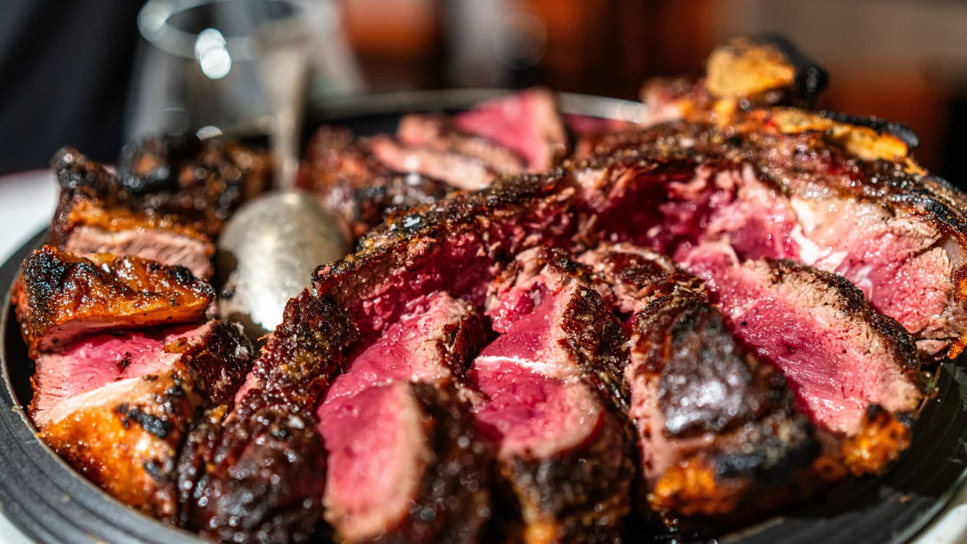 A close-up view of a plate featuring a thick cut of Florentine Steak (Bistecca alla Fiorentina), a traditional Italian T-bone steak, typically served rare and sliced, with a garnish of herbs.