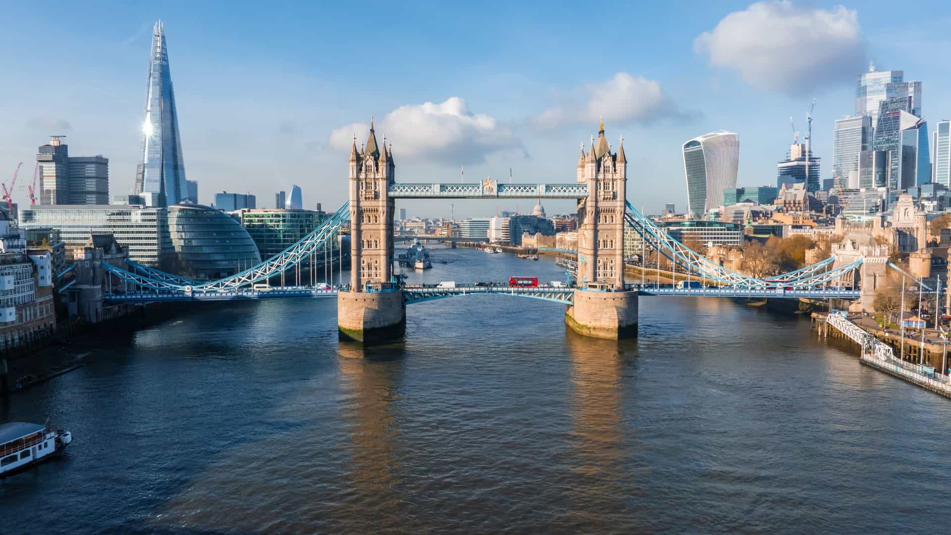 An aerial view of the iconic Tower Bridge in London, England, connecting the city of London with Southwark across the River Thames. The image captures the bridge's distinctive twin towers and the suspended central section, along with the surrounding cityscape.