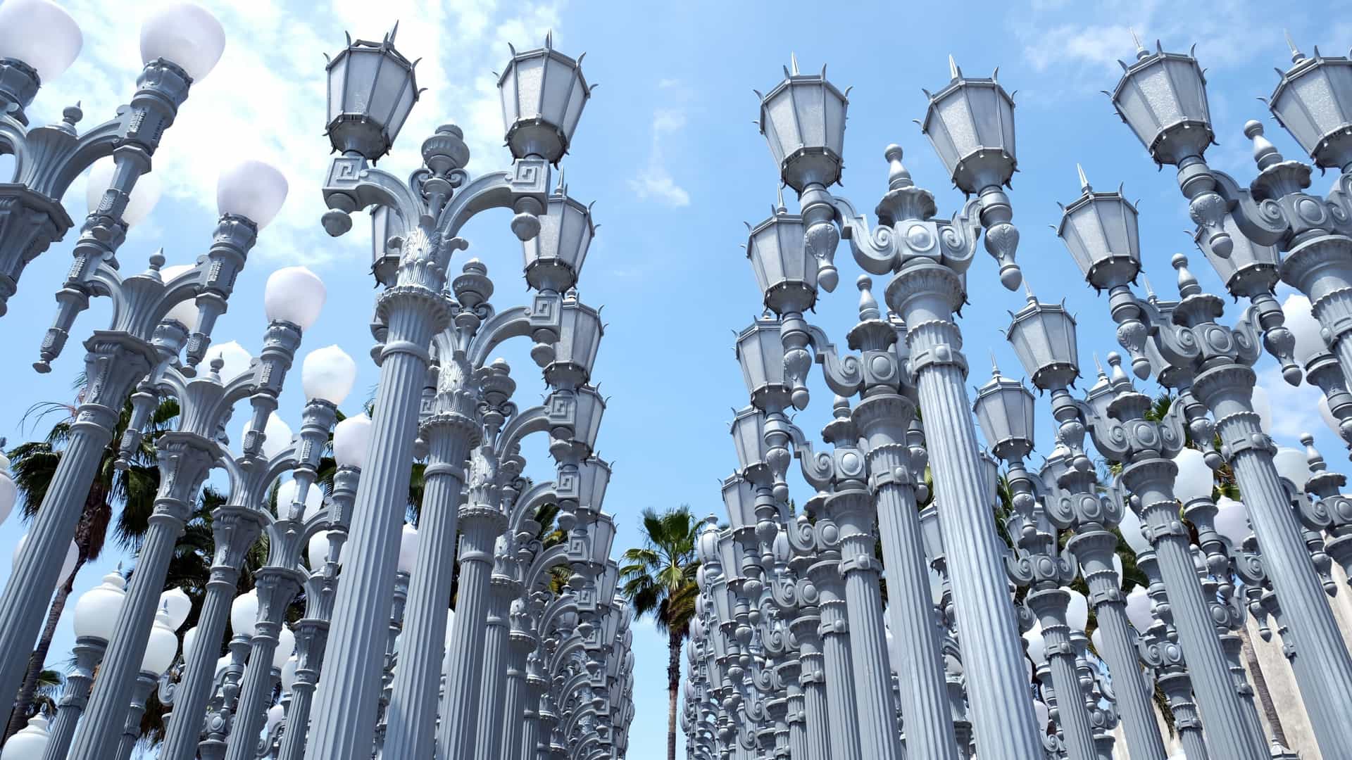 A dense, grid-like arrangement of over 200 restored, gray-painted cast iron antique street lamps, known as the "Urban Light" installation by artist Chris Burden, standing illuminated at the Wilshire Boulevard entrance of the Los Angeles County Museum of Art (LACMA).