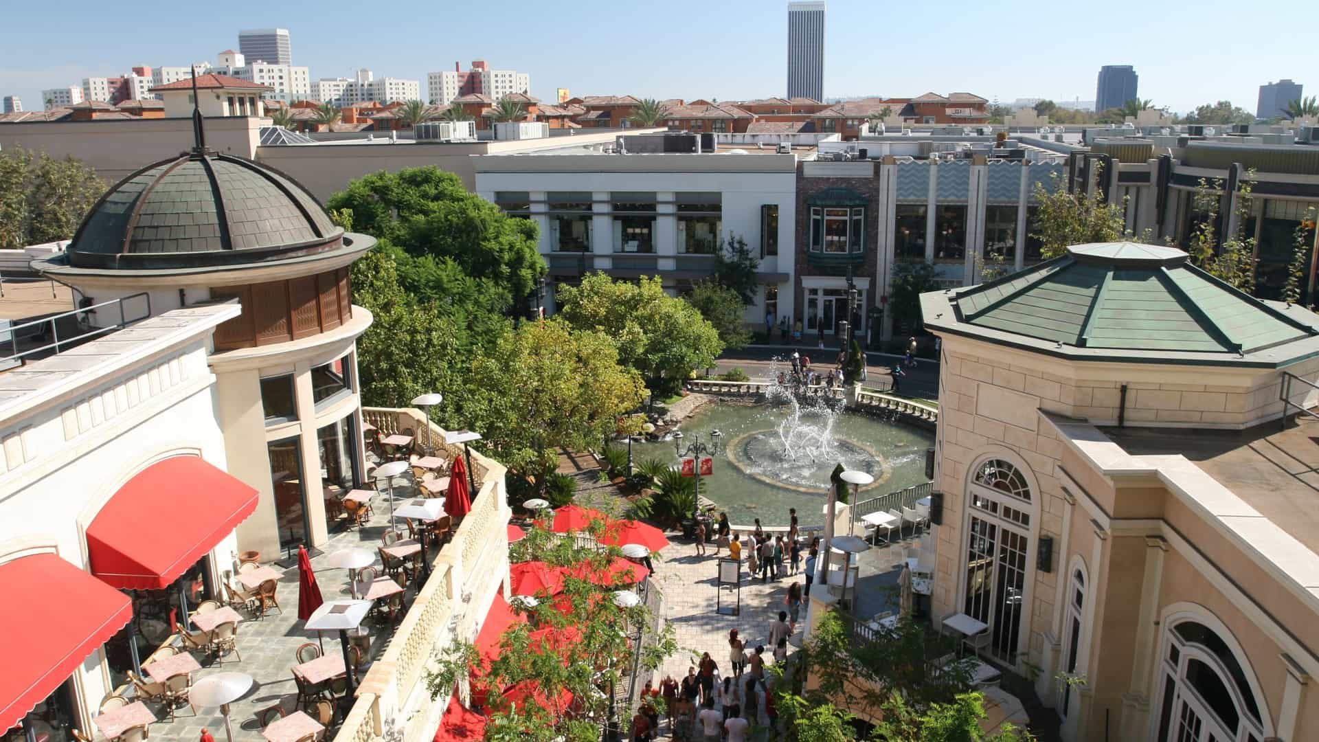 A scenic view of The Grove, a beautiful open-air shopping center in Los Angeles, California, designed with a classic, urban town square aesthetic featuring a central fountain and stylish, low-rise retail buildings.