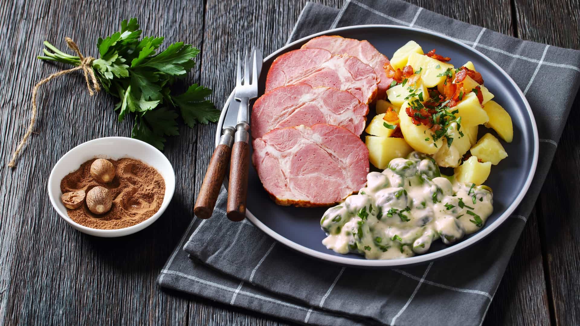 Close-up view of Judd mat Gaardebounen, the national dish of Luxembourg. The plate holds several slices of savory smoked pork collar and a side of broad beans in a creamy, light-colored sauce, often served with boiled potatoes.